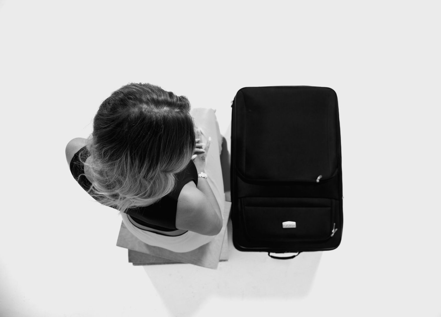 Aerial view of person sitting next to black luggage against white background.