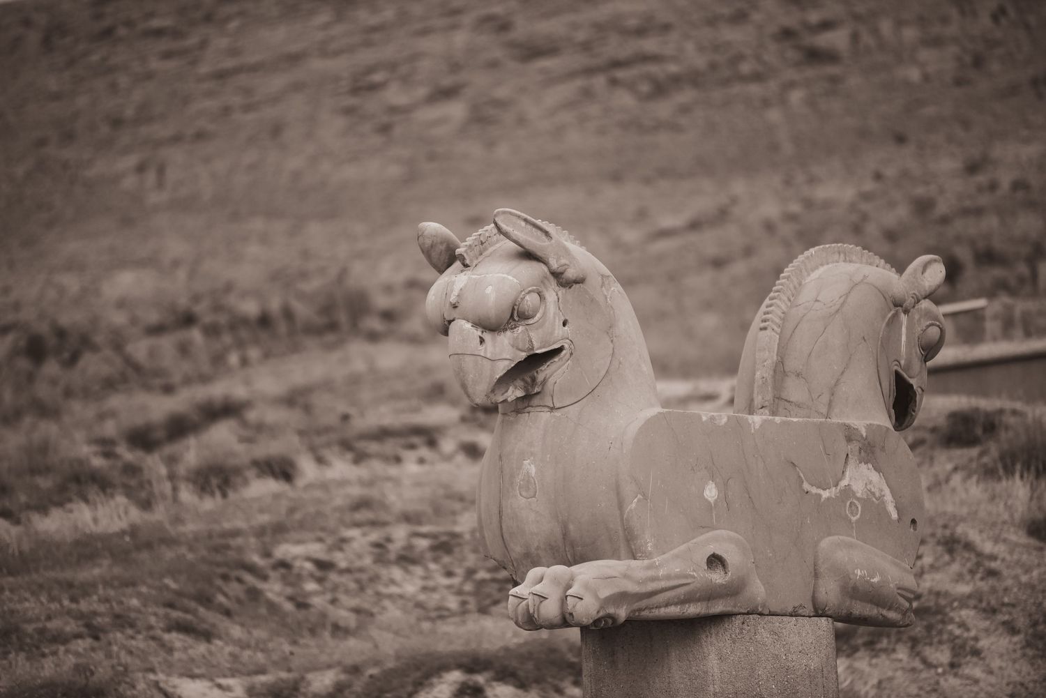 Stone carved lion sculpture in sepia tones against rugged landscape.