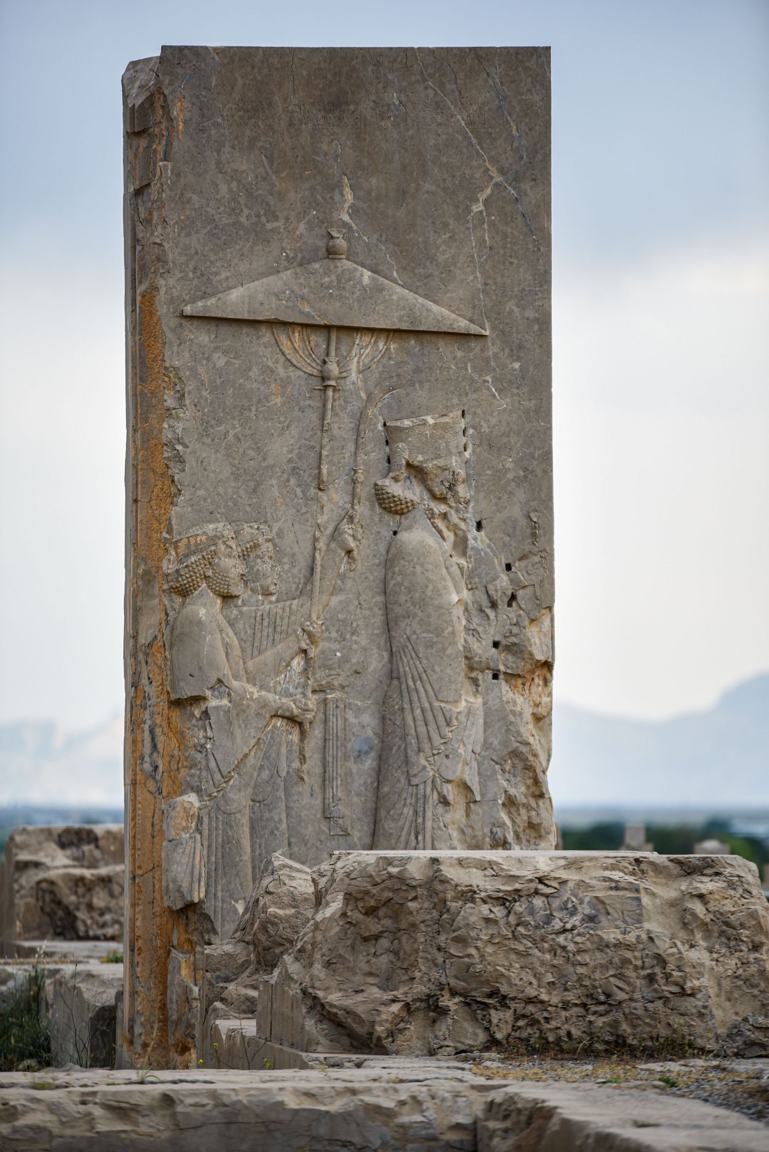 Ancient Persian stone relief carving showing figures under an umbrella-like parasol.