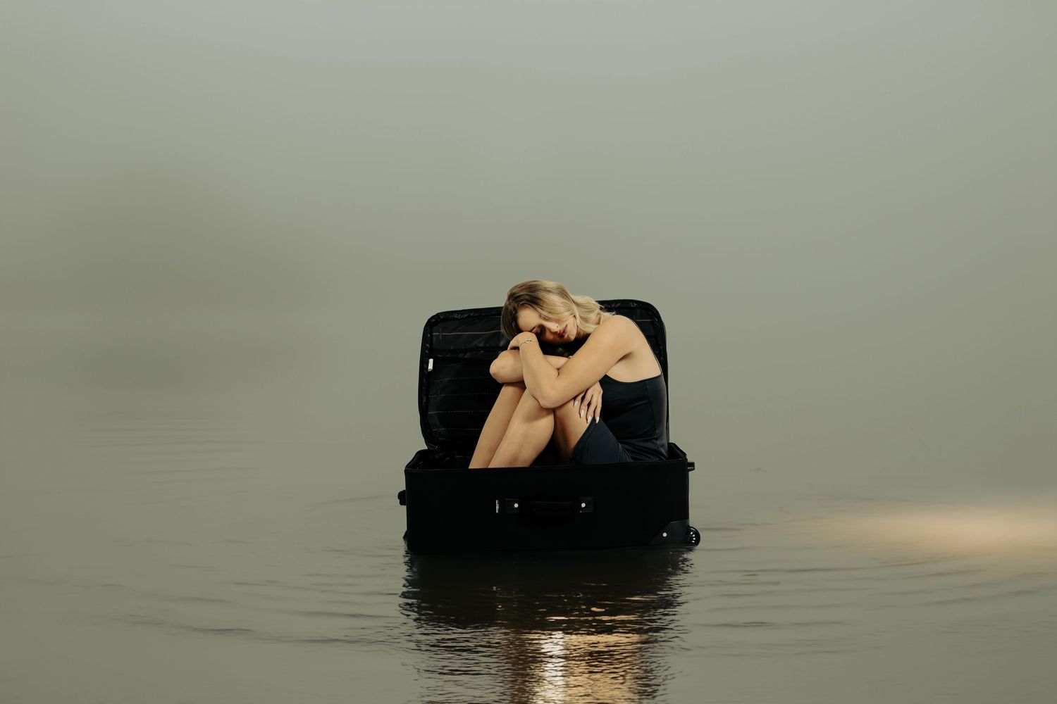 Silhouette on floating suitcase in misty water during golden hour.