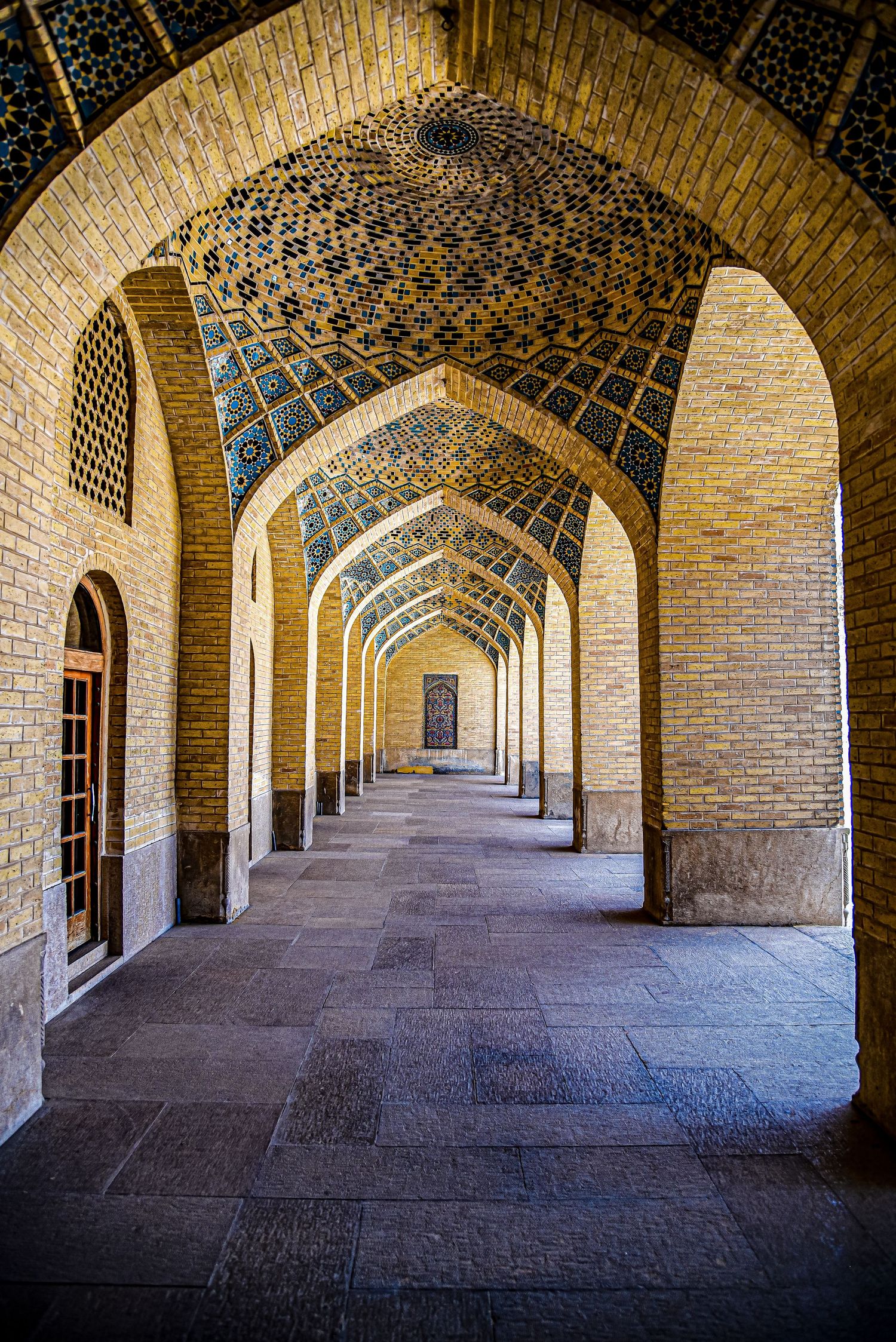 Arched corridor in historic mosque showing repeating vaulted ceiling with geometric tile patterns.