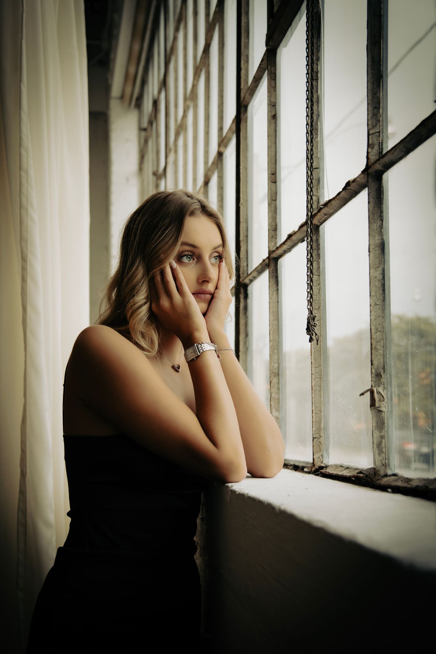Atmospheric portrait by a window with soft natural lighting and vintage curtains.