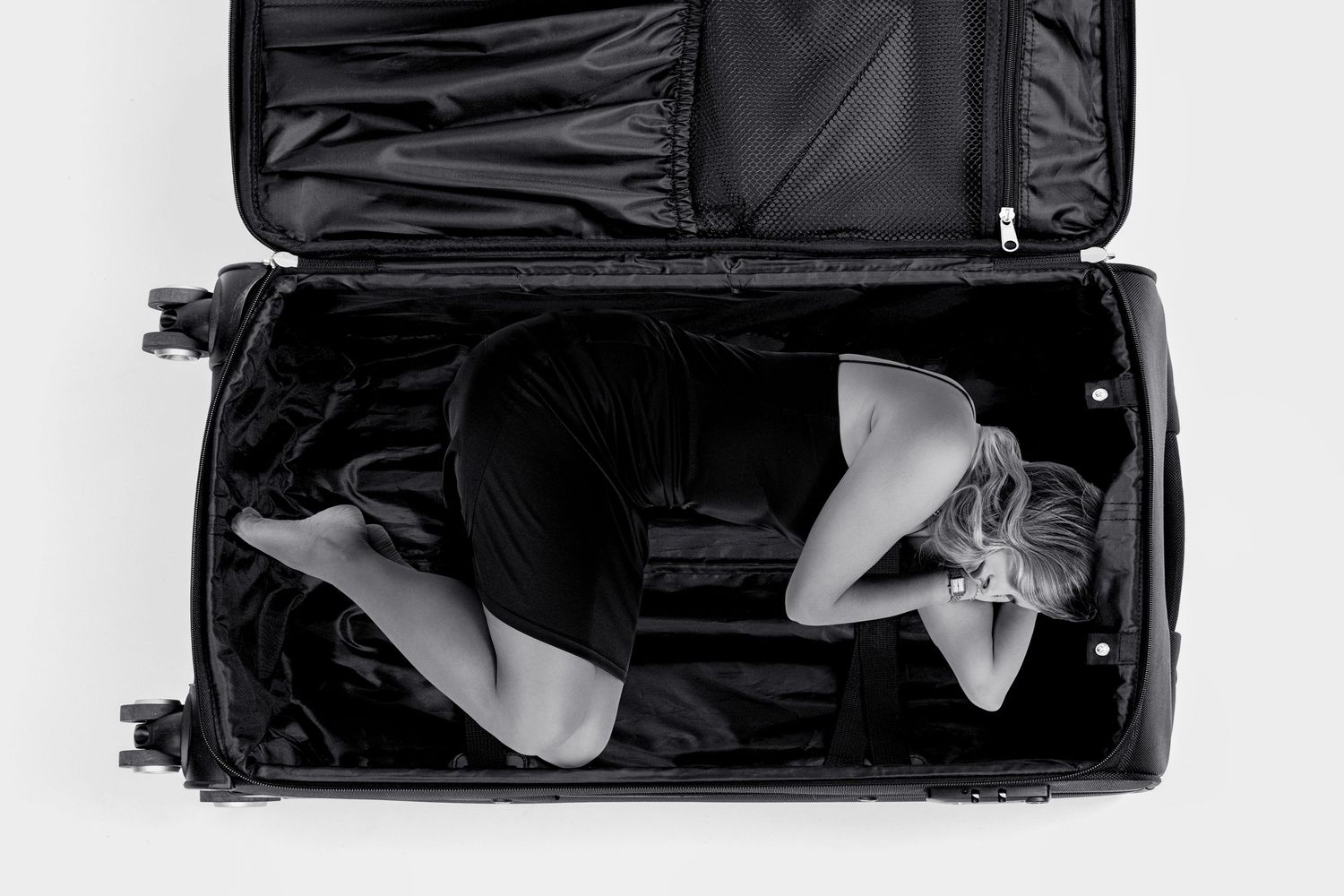 Woman lying inside an open black suitcase in artistic black and white photography.