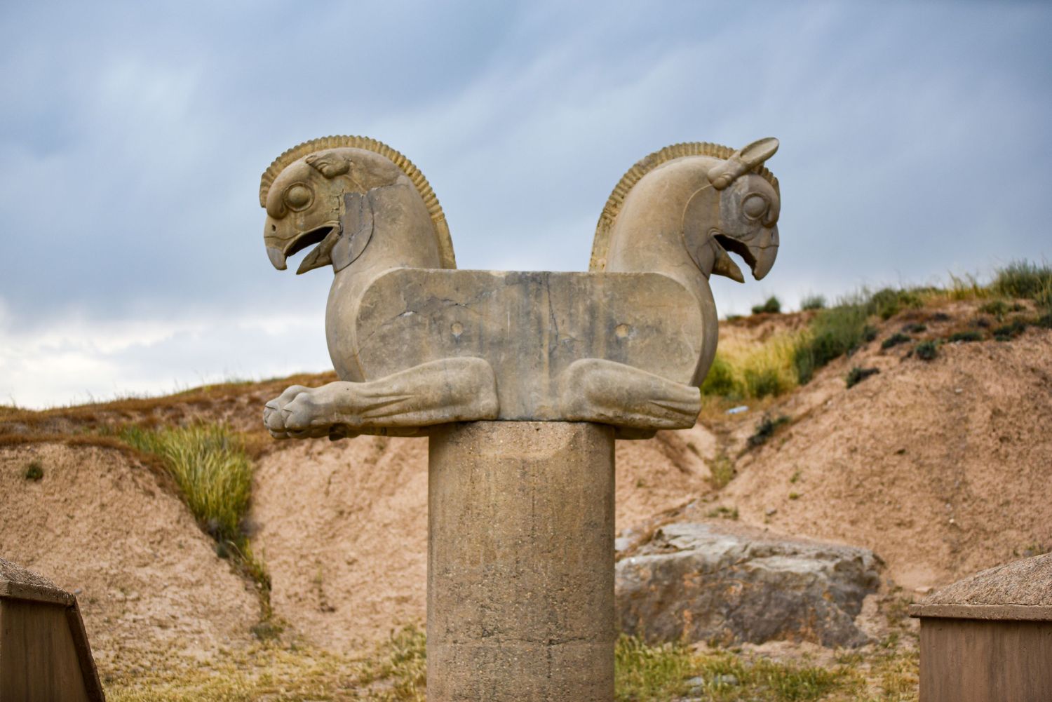 Stone column topped with carved double-headed horse sculpture at ancient Persian ruins.