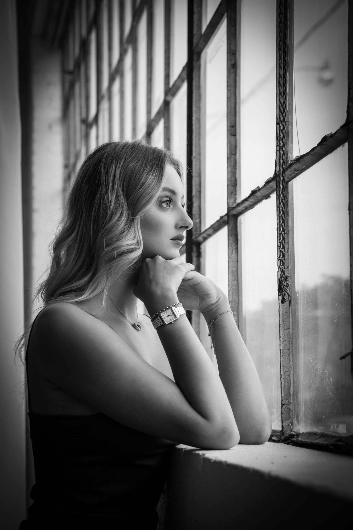 Black and white artistic portrait showing contemplative pose by a window.
