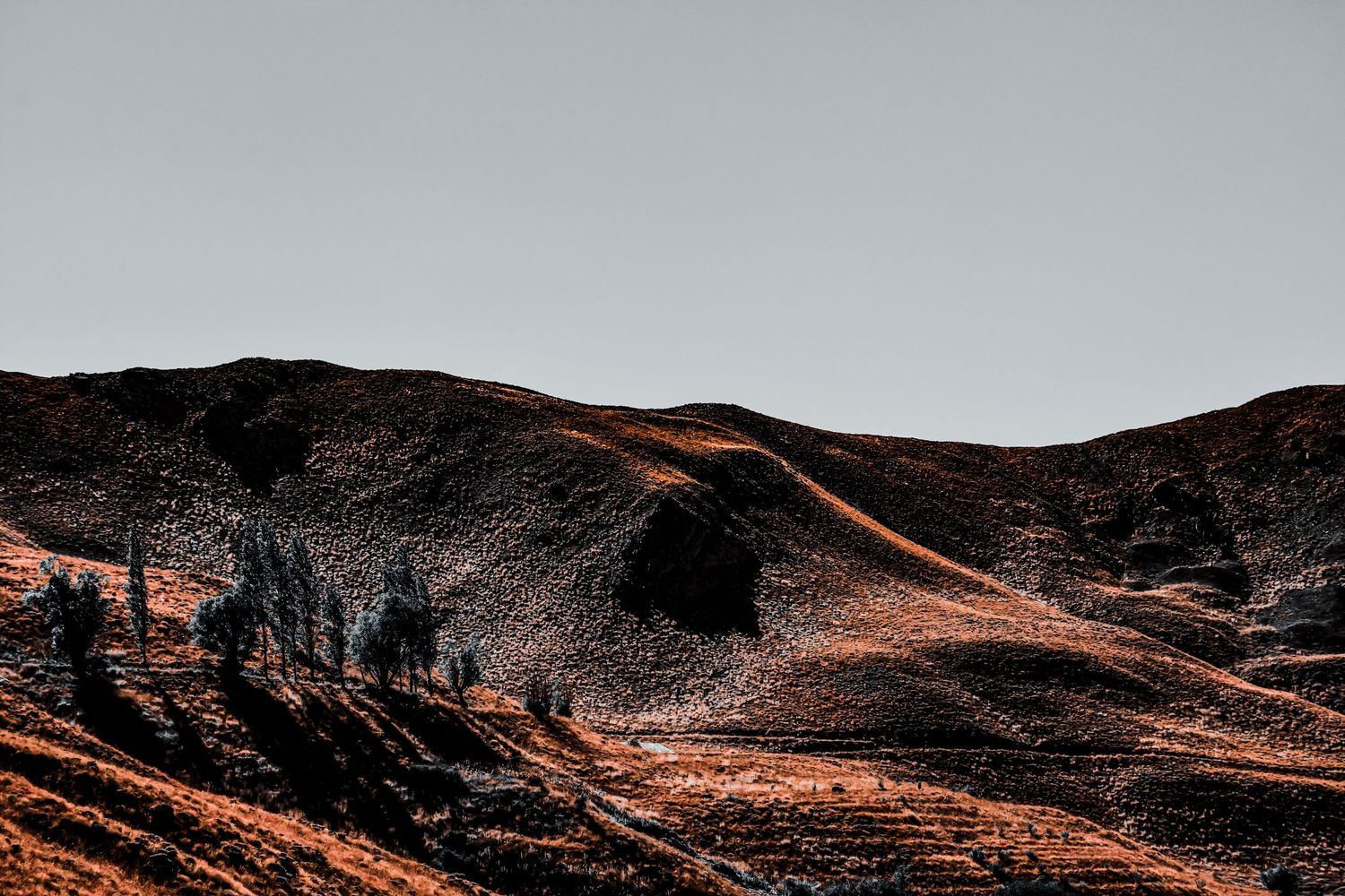 Rugged mountain landscape with winding trails in copper and dark tones at sunset.