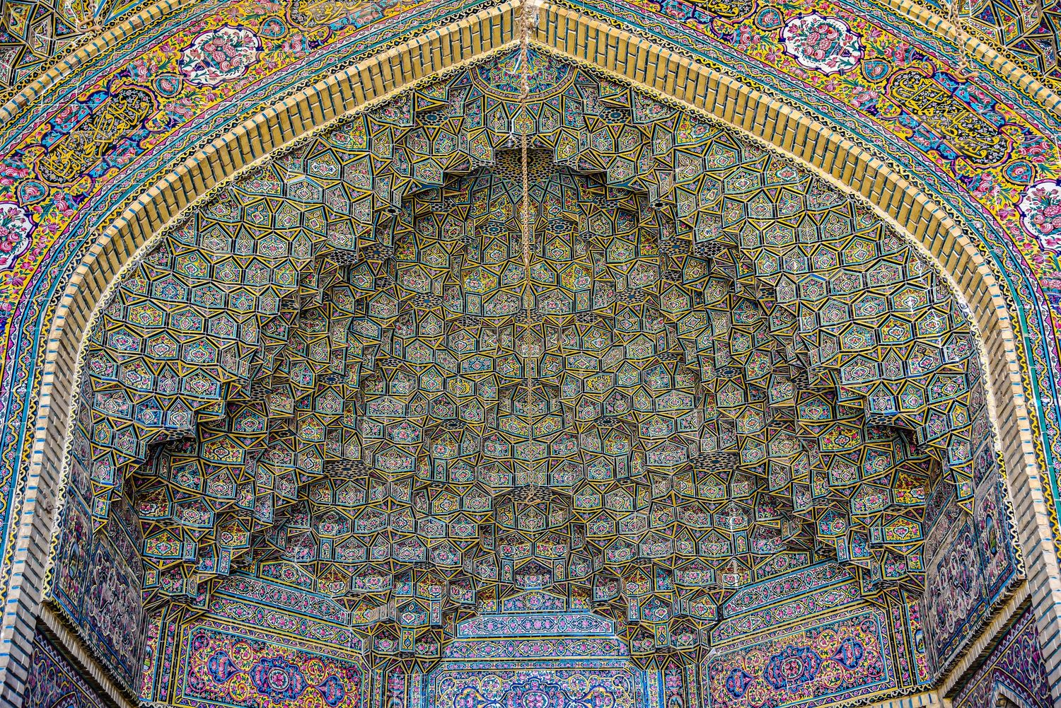 Elaborate muqarnas honeycomb vaulting decorated with geometric patterns in green and gold.