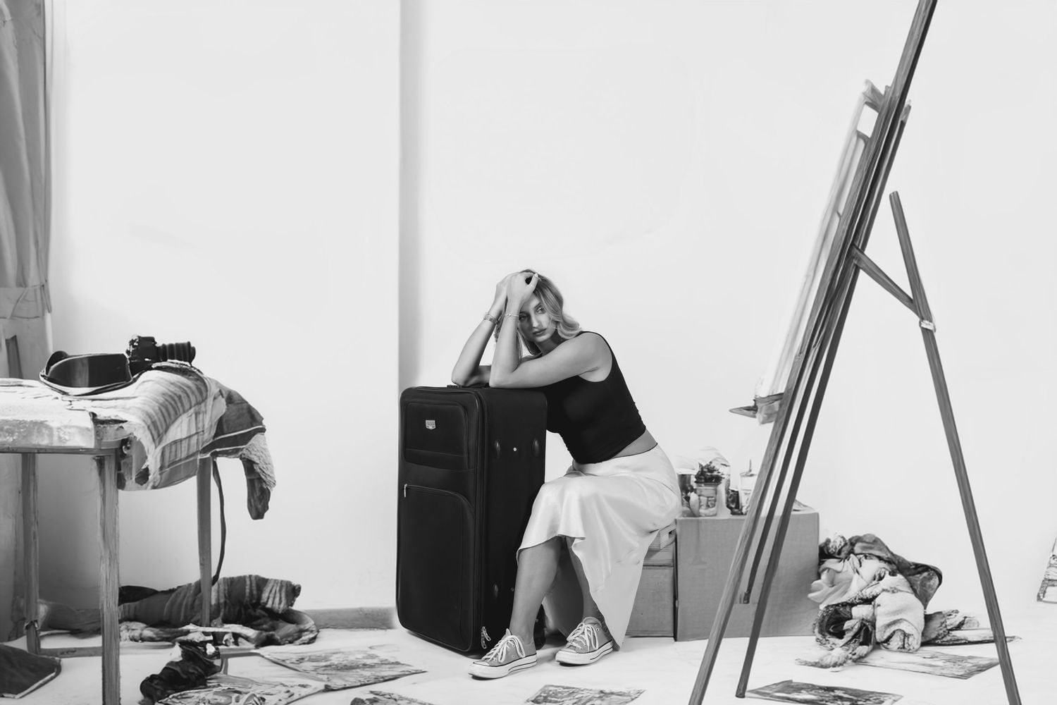 Black and white image of figure sitting in messy room with ladder and personal items.