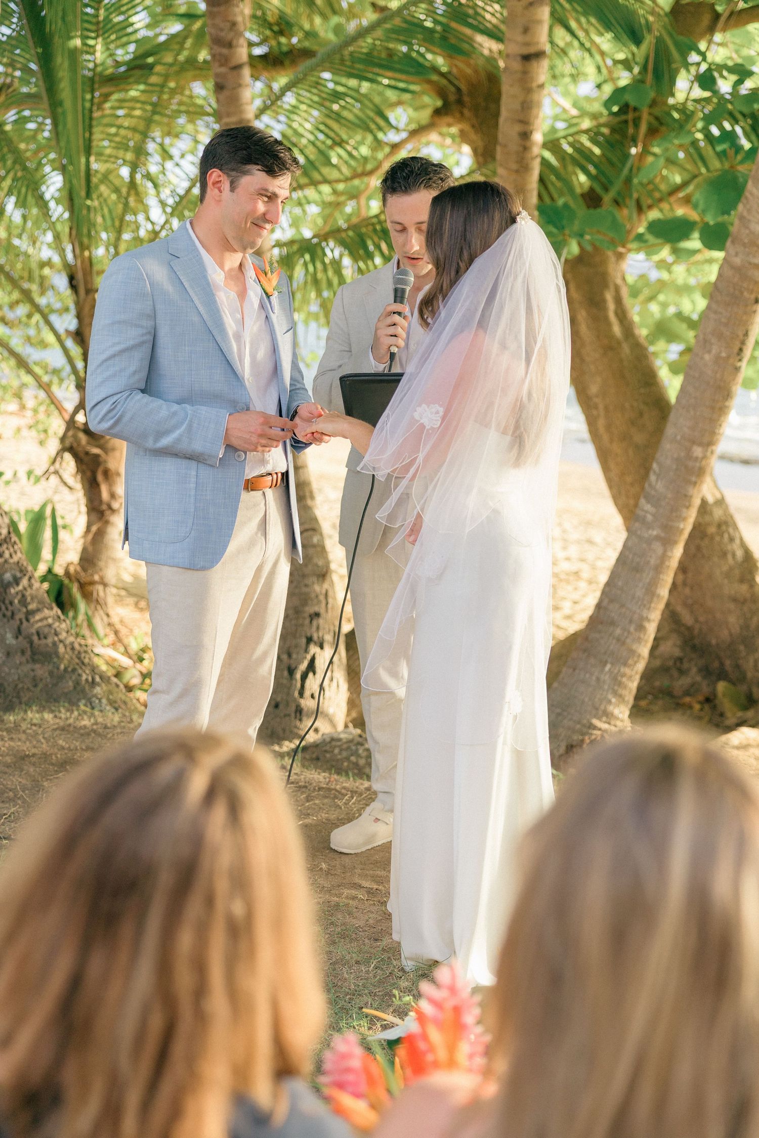 Couple exchanging vows during outdoor ceremony beneath palm trees.