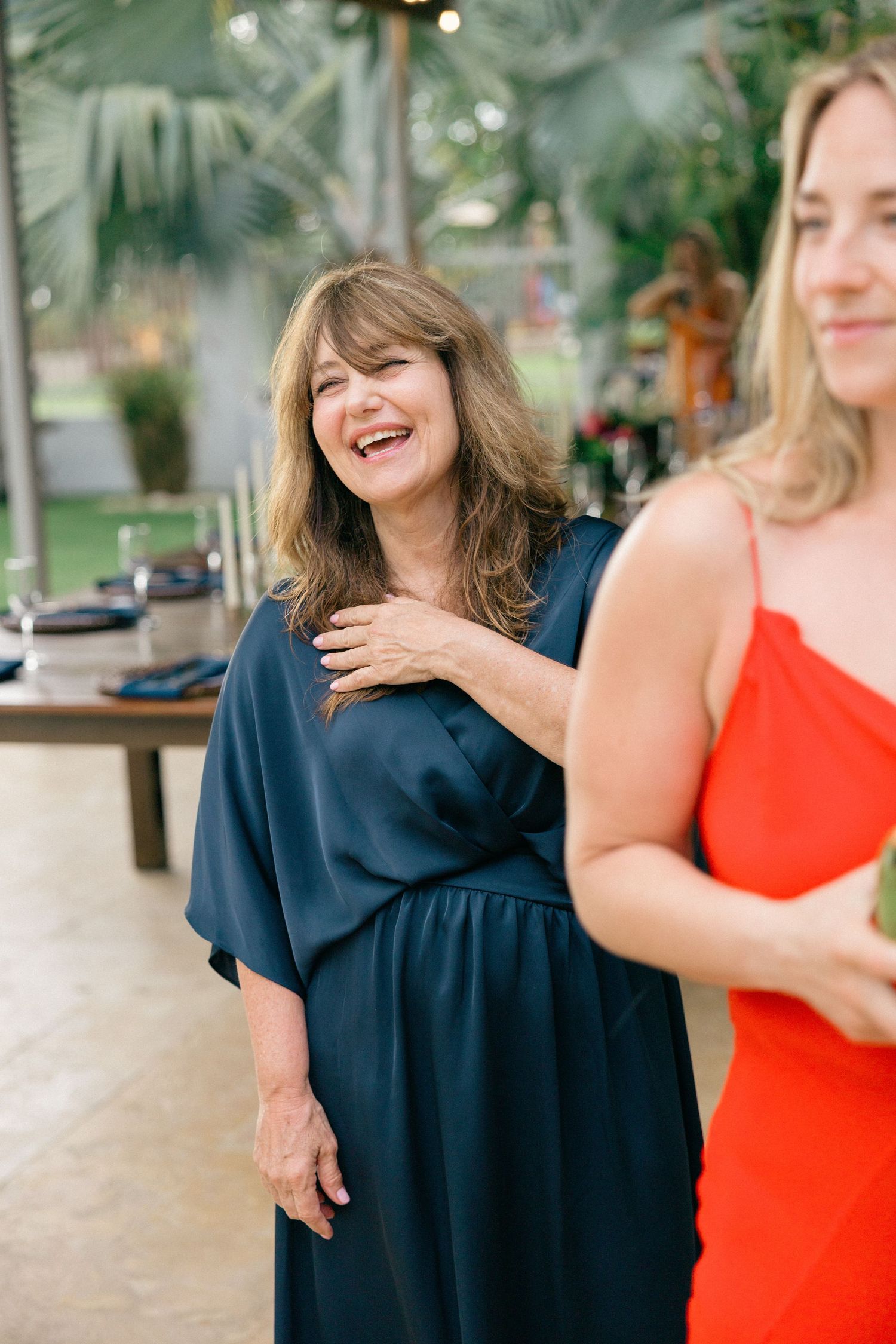 Two women sharing a joyful moment at an outdoor tropical venue.