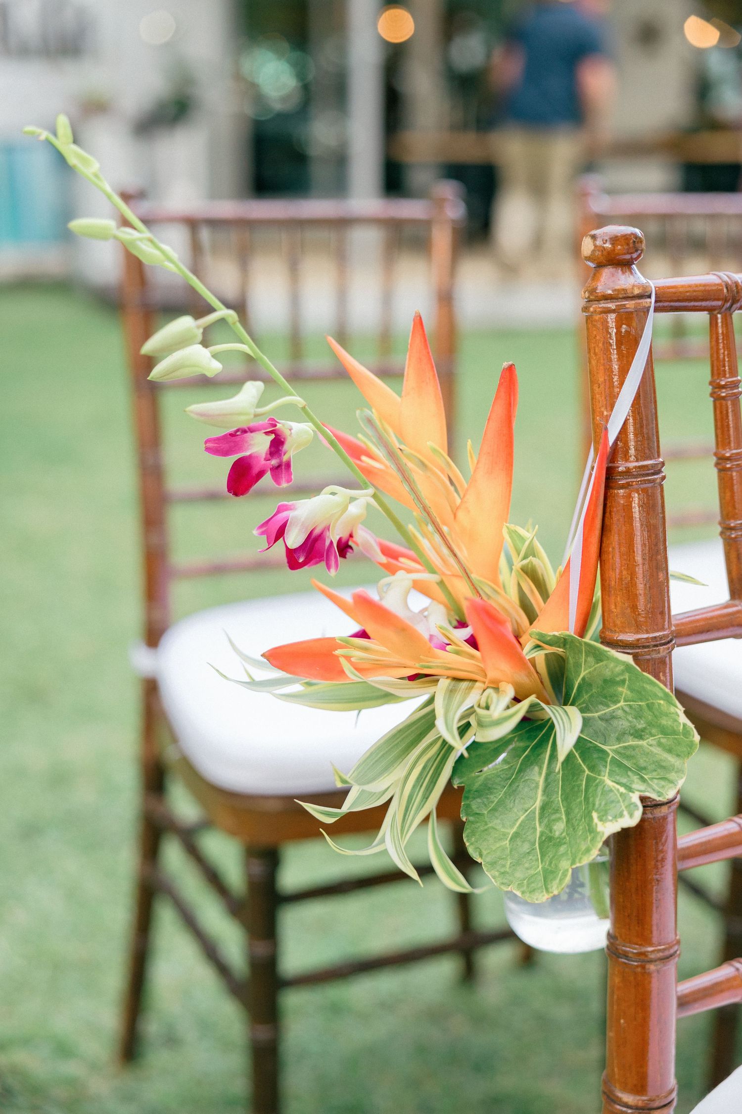 Wooden ceremony chairs decorated with tropical flowers and birds of paradise arrangements.