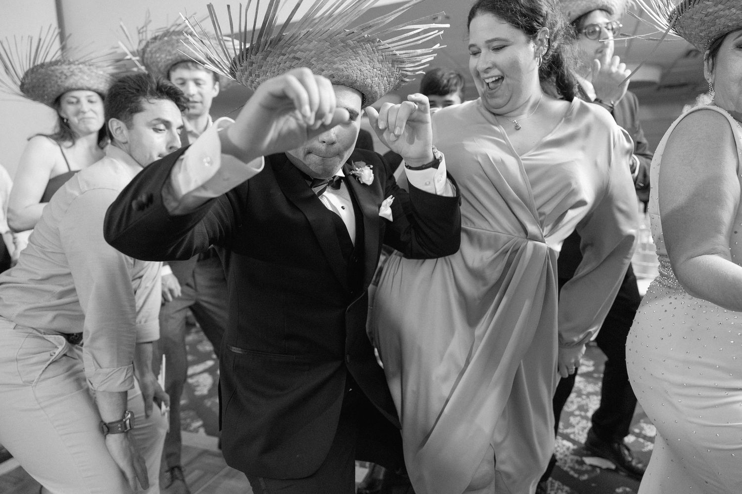Wedding guests dance in a line formation at an indoor reception venue.