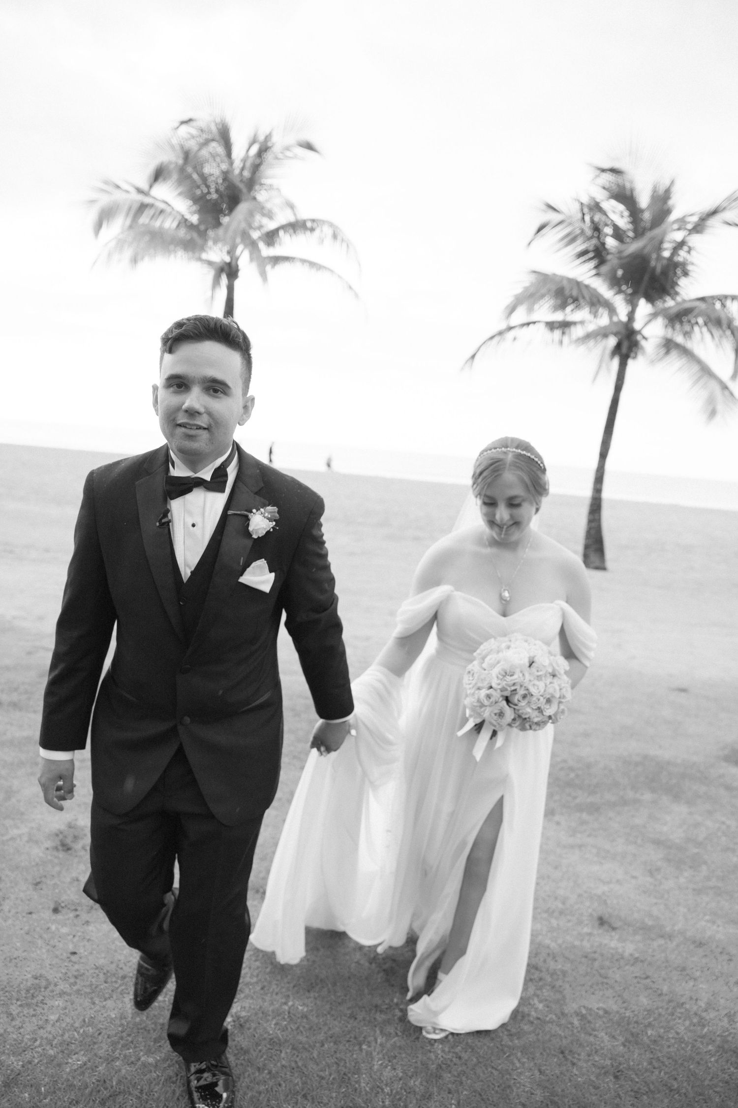 Playful black and white photos of newlyweds running on grass with palm trees.