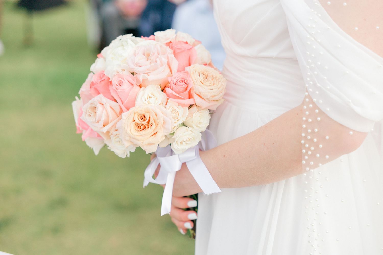 Beautiful peach and pink rose wedding bouquet held against a white dress.
