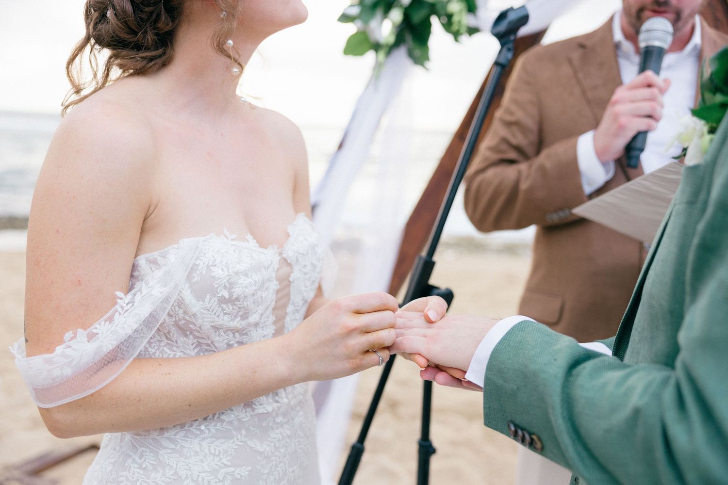 Exchange of rings during beach wedding ceremony with microphone stand visible.