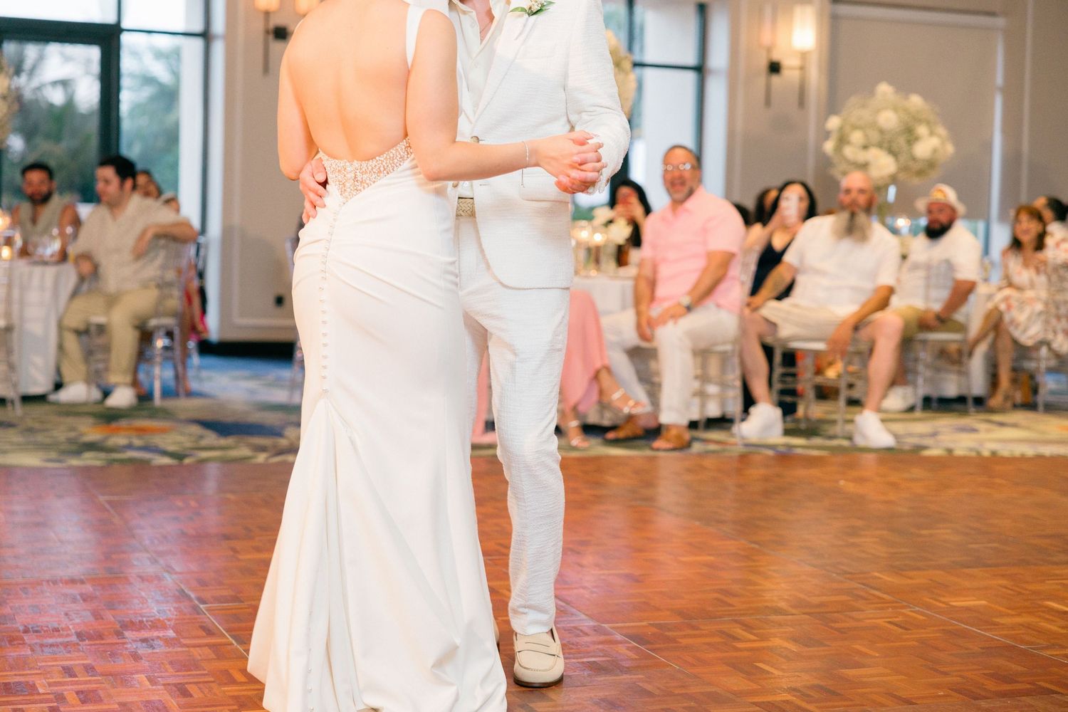 A couple shares an intimate dance moment on a wooden floor at their wedding reception.
