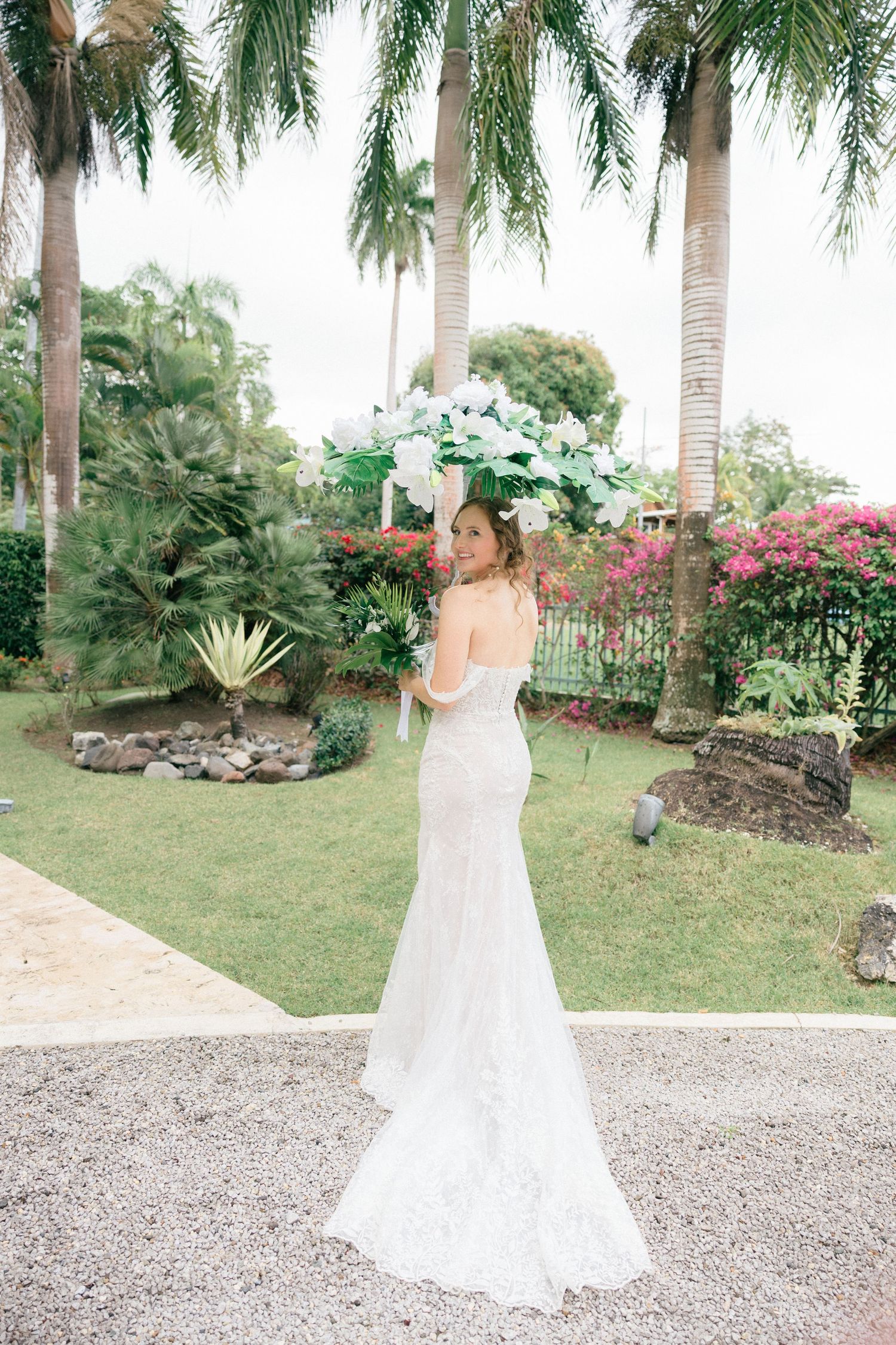 Bride in flowing white dress poses in a tropical garden setting with palm trees.