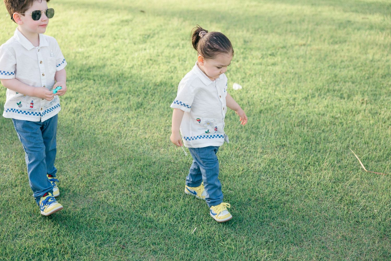 Young child walks on grassy lawn wearing jeans and white shirt.