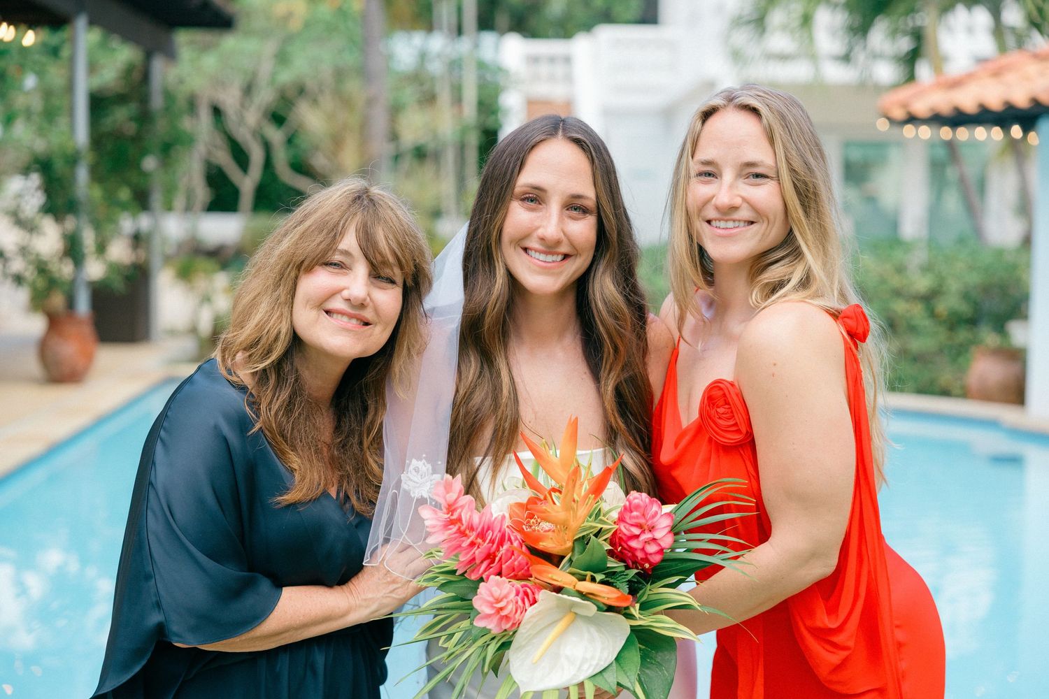 Wedding party celebrates with joyful poses by a poolside surrounded by palm trees.