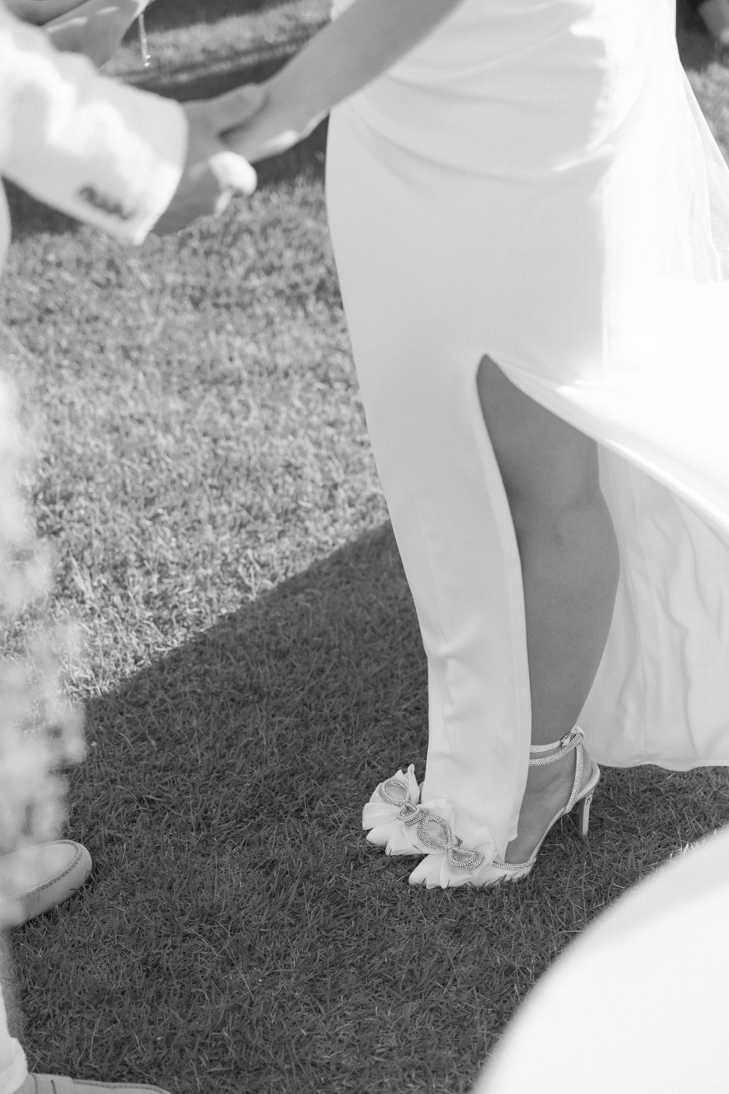 Close-up of bride's white dress and shoes on grass during wedding.