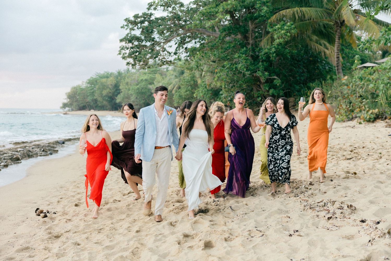 People gathered on a tropical beach with palm trees and colorful attire for a group photo.