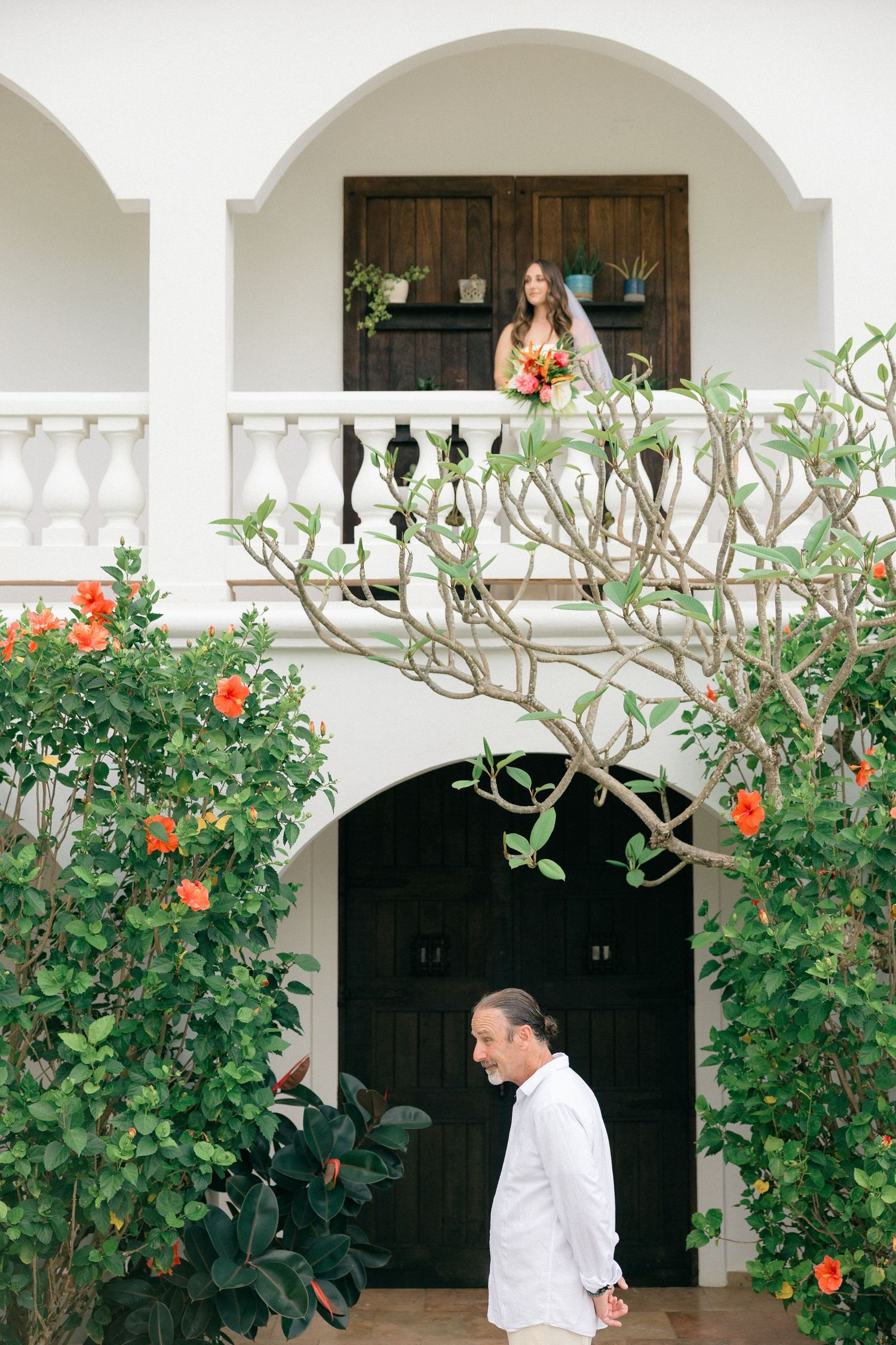 Mediterranean-style white building with arched balconies and flowering plants framing a dark wooden door.