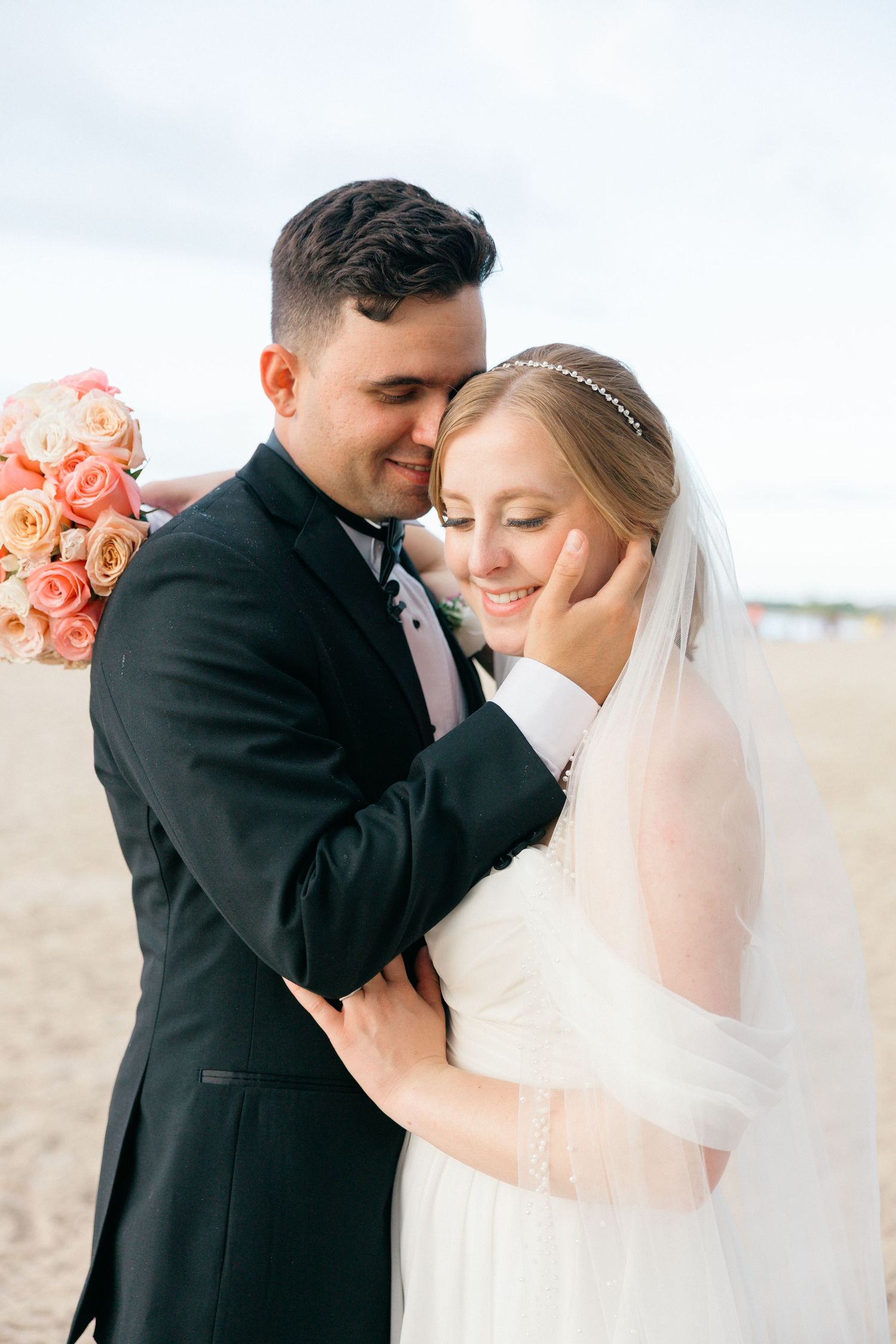 Tender wedding moments captured on beach with coral floral bouquet details.