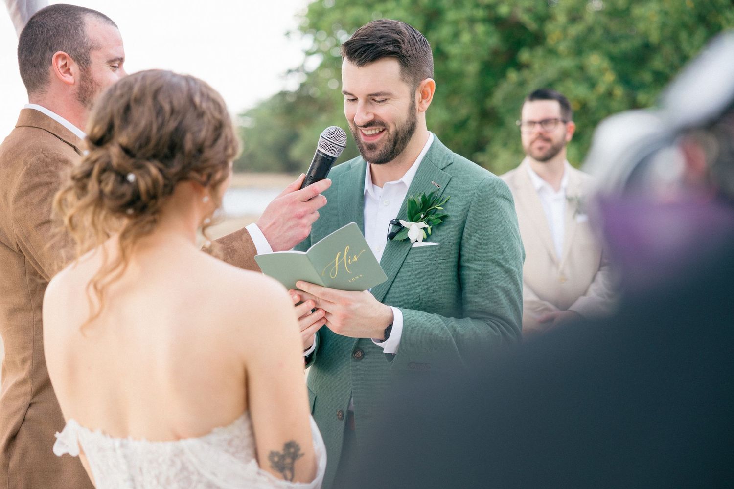 Wedding party gathered outdoors in green and grey attire.