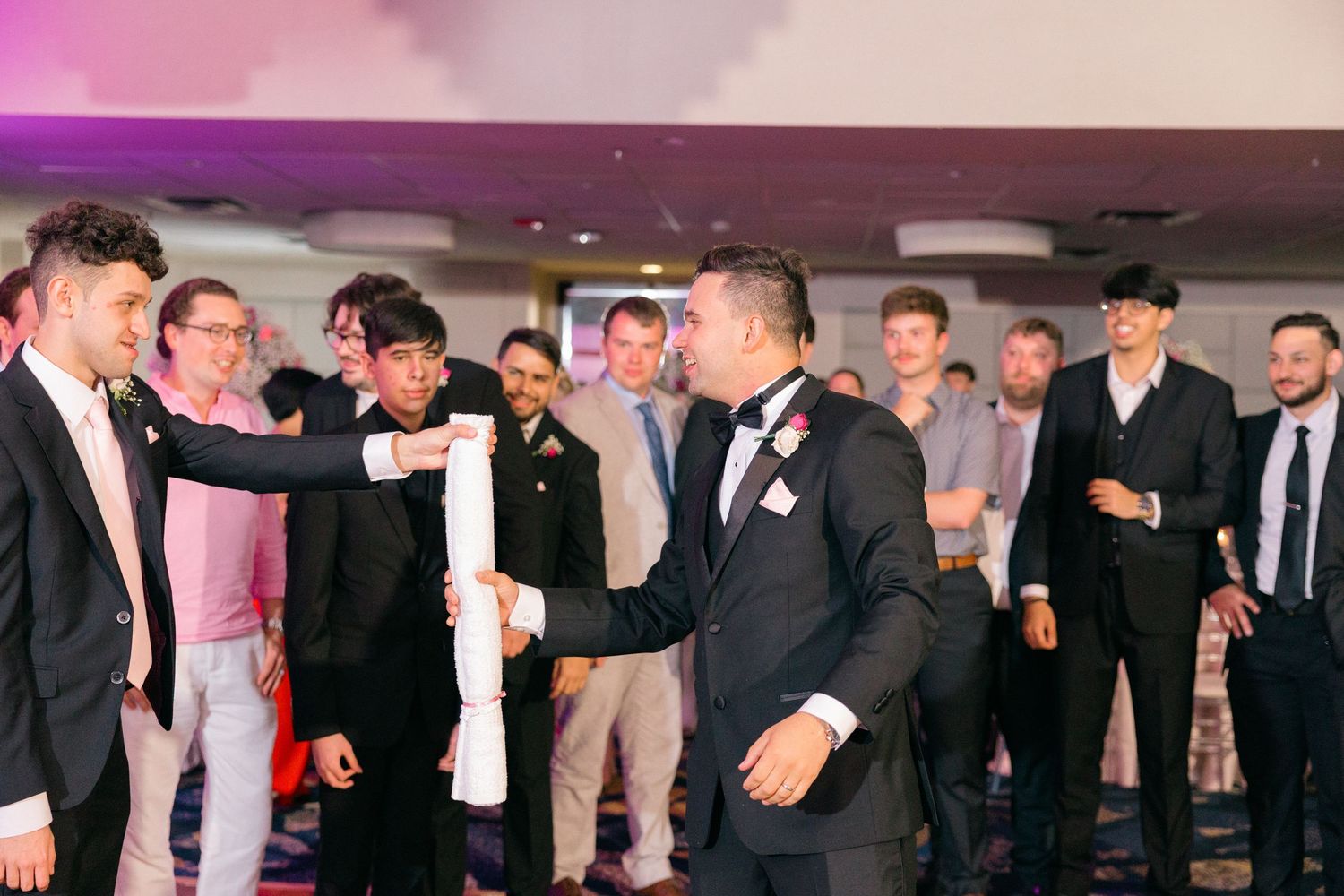 Wedding guests dancing and celebrating under colorful lighting at an evening reception.
