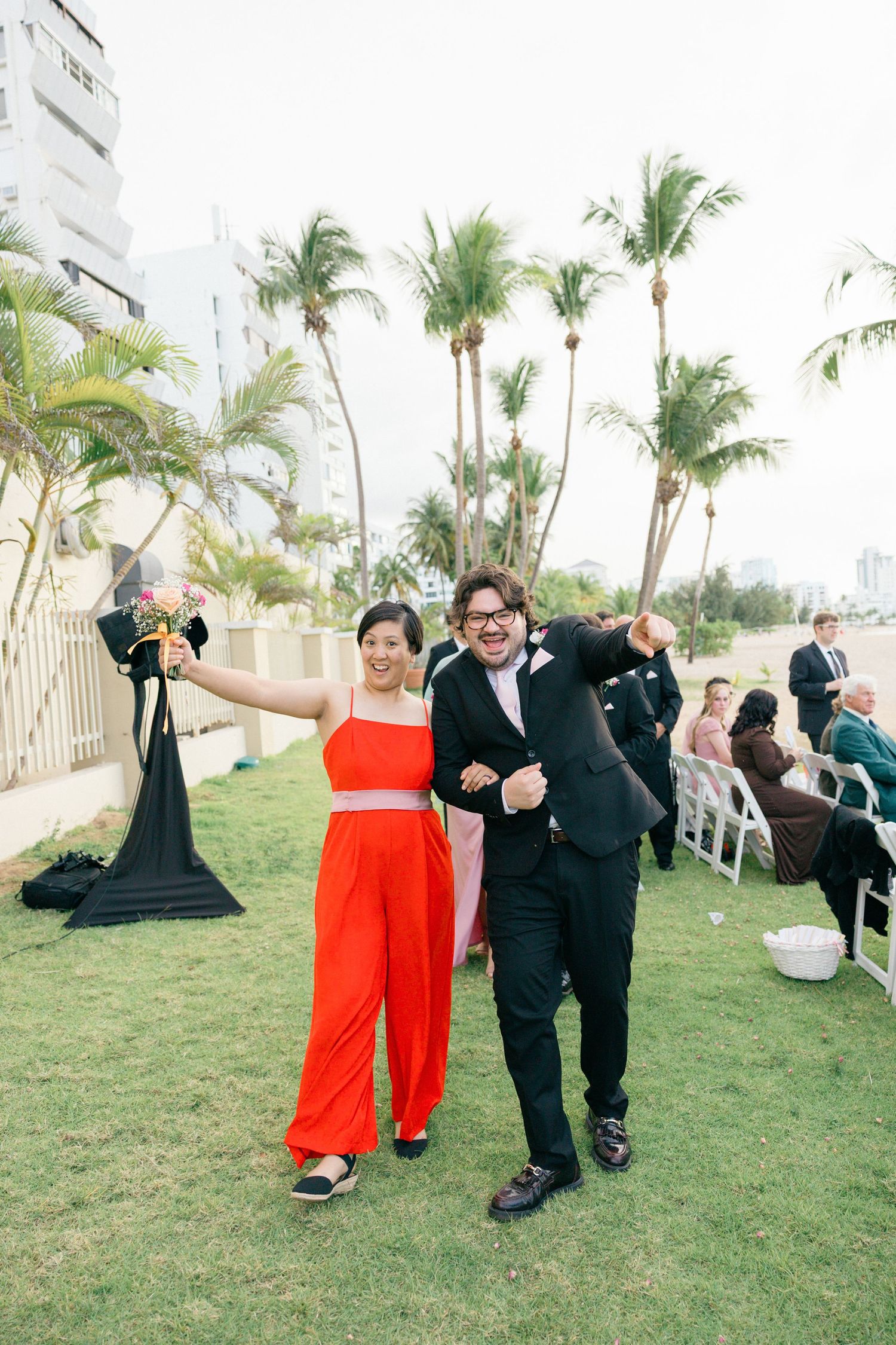 Wedding party members walk joyfully across lawn during outdoor celebration.