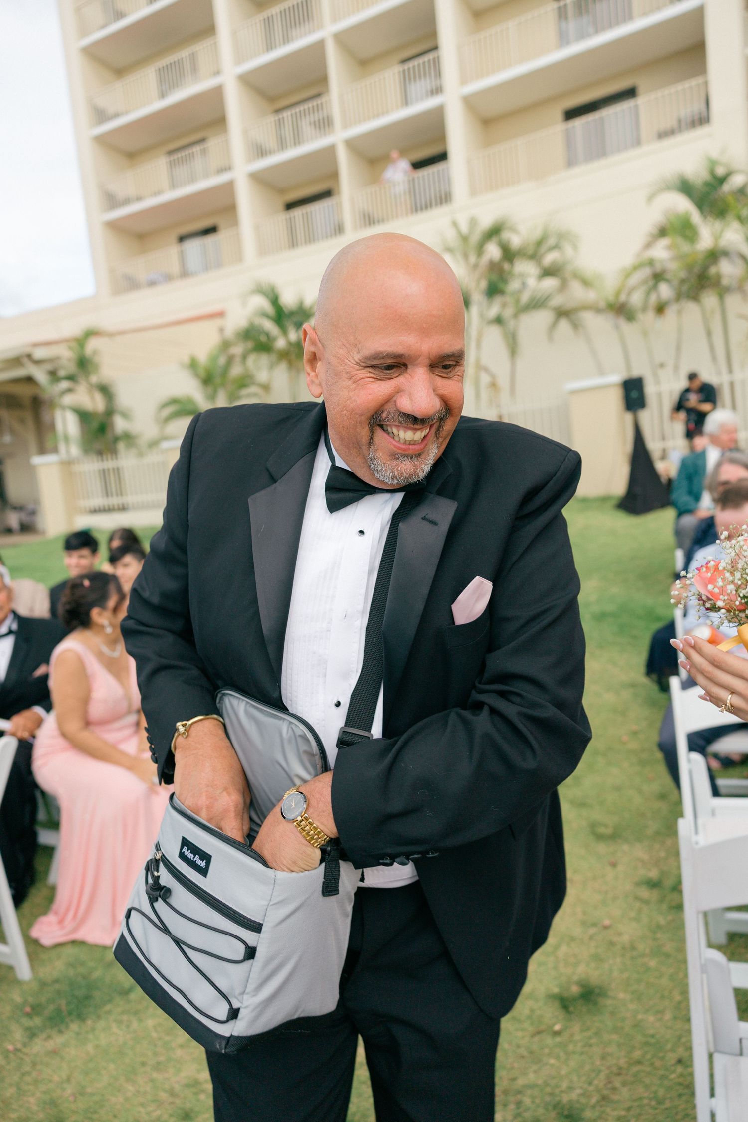 Groomsman in tuxedo wearing baseball glove at outdoor wedding ceremony.