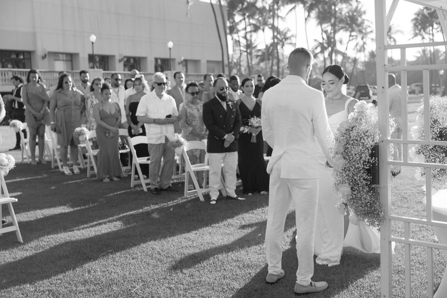Black and white photo of wedding guests gathered on a lawn during an outdoor ceremony.