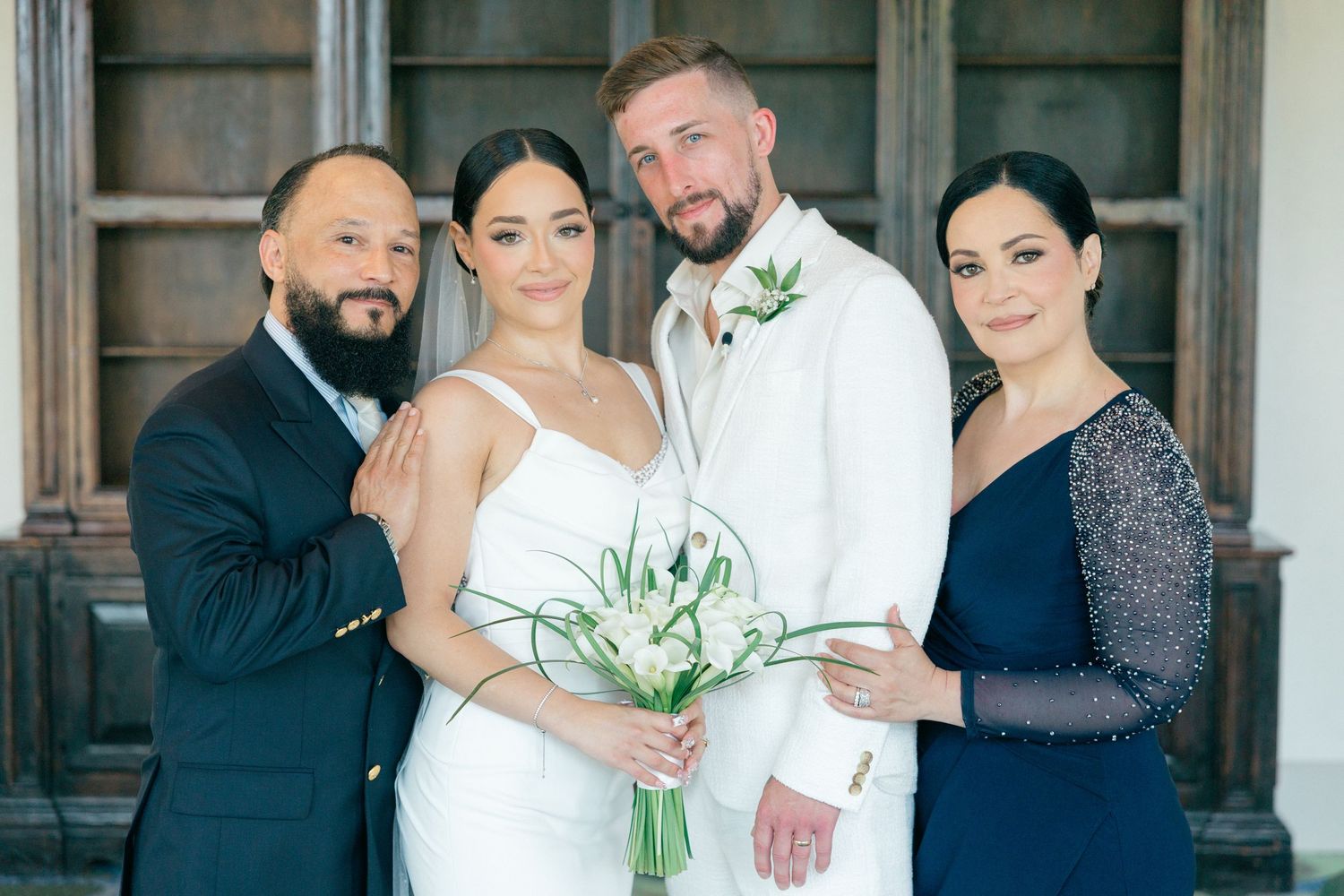 Wedding party posing together in formal attire against rustic architectural backdrop.