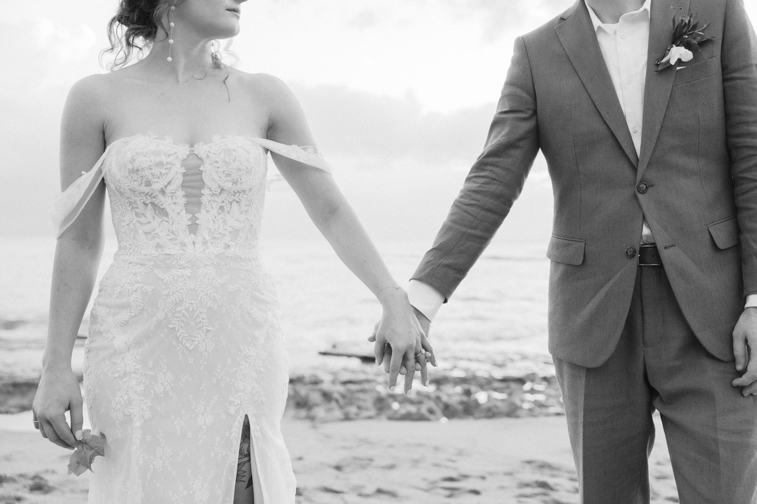 Elegant wedding couple poses against ocean backdrop in formal attire.