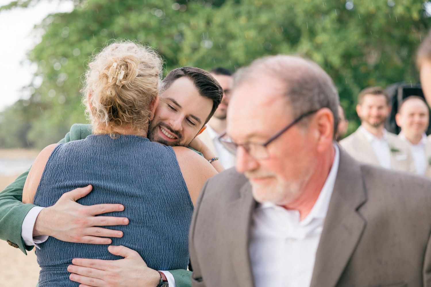 Wedding guests embrace and share emotional moments during an outdoor celebration.