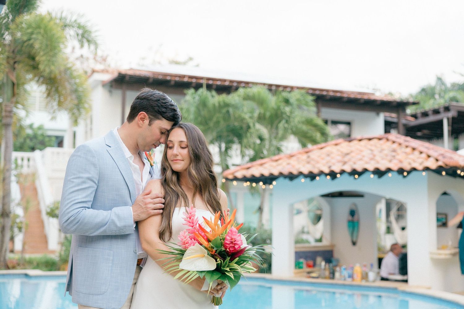 Couple shares an intimate moment by a pool with Spanish-style architecture and tropical flowers.
