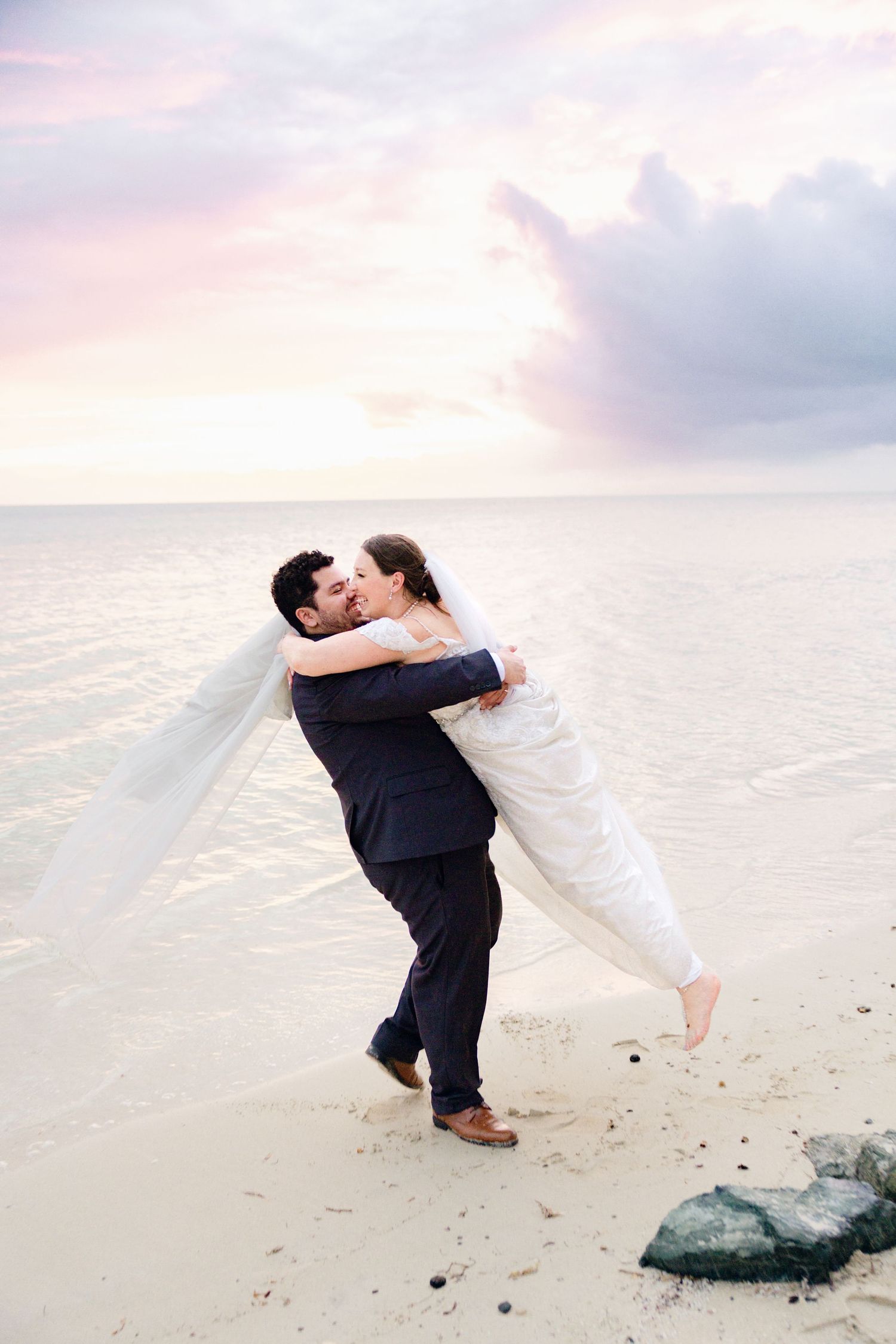 Romantic beach photoshoot with couple in wedding attire at sunset.