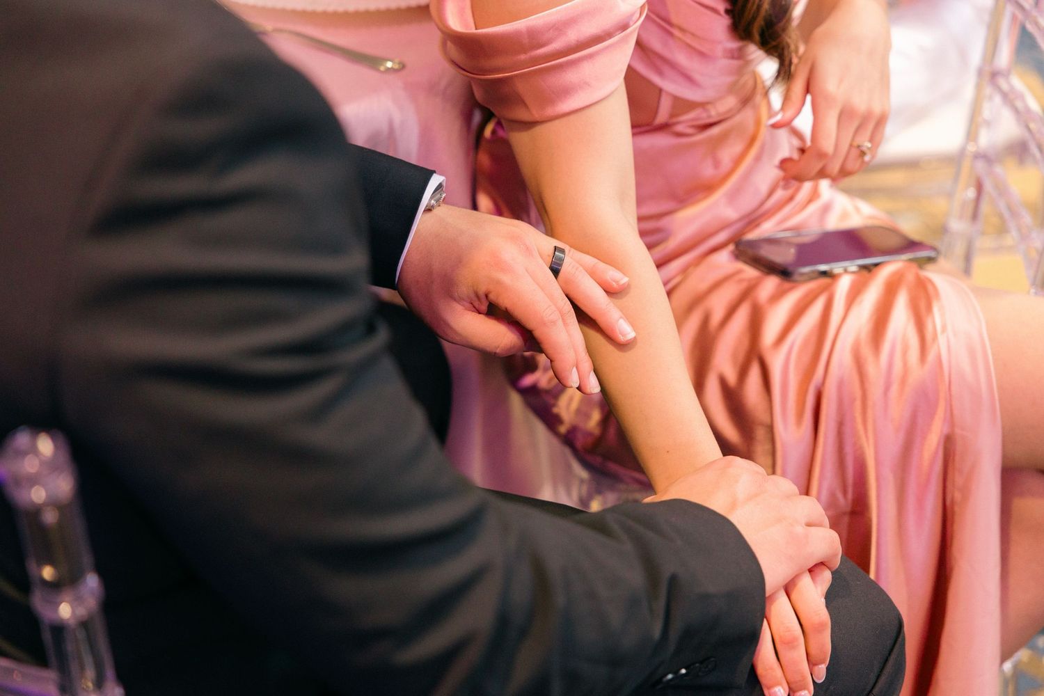 Close-up of hands touching during an intimate moment at a wedding with pink dress details.