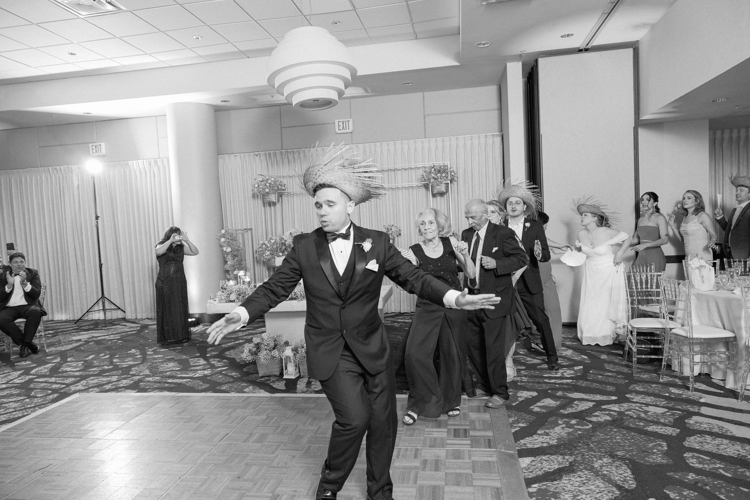 Black and white photo of wedding guests dancing in a reception hall with checkered floor.