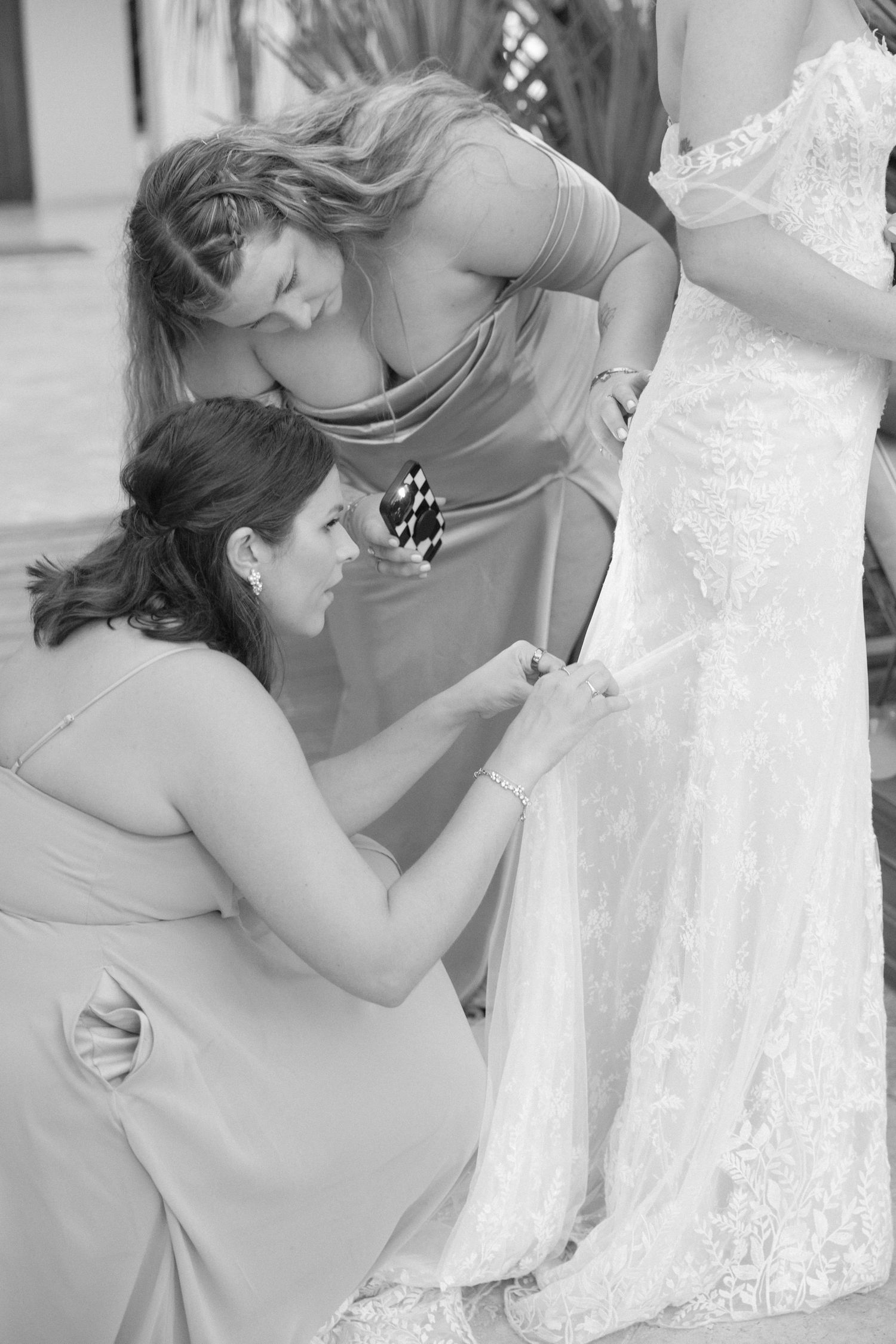 Black and white photos show a close-up of someone adjusting details on an elegant white wedding dress.