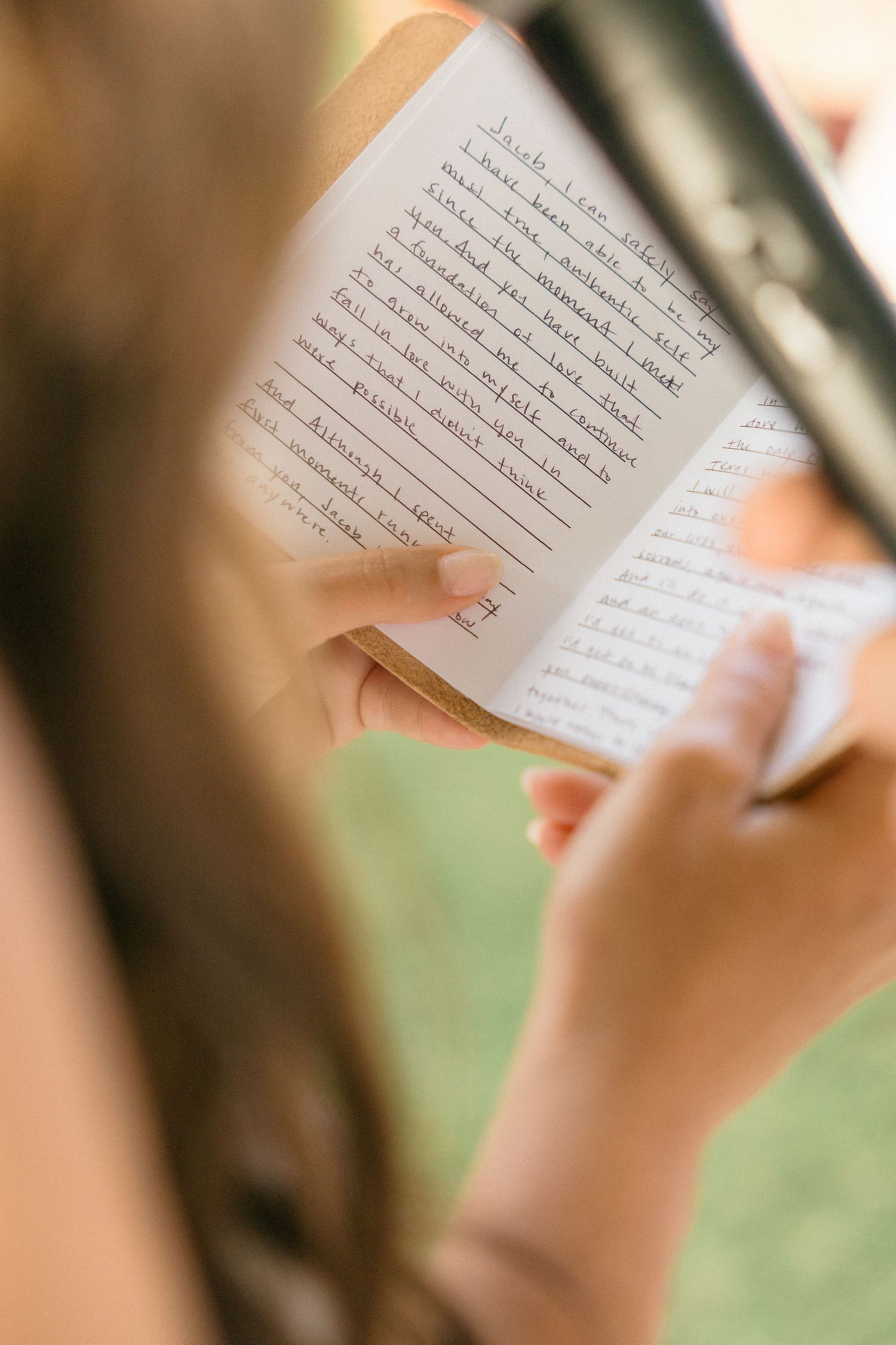 Close-up shot of hands holding a wedding ceremony program or reading material outdoors.