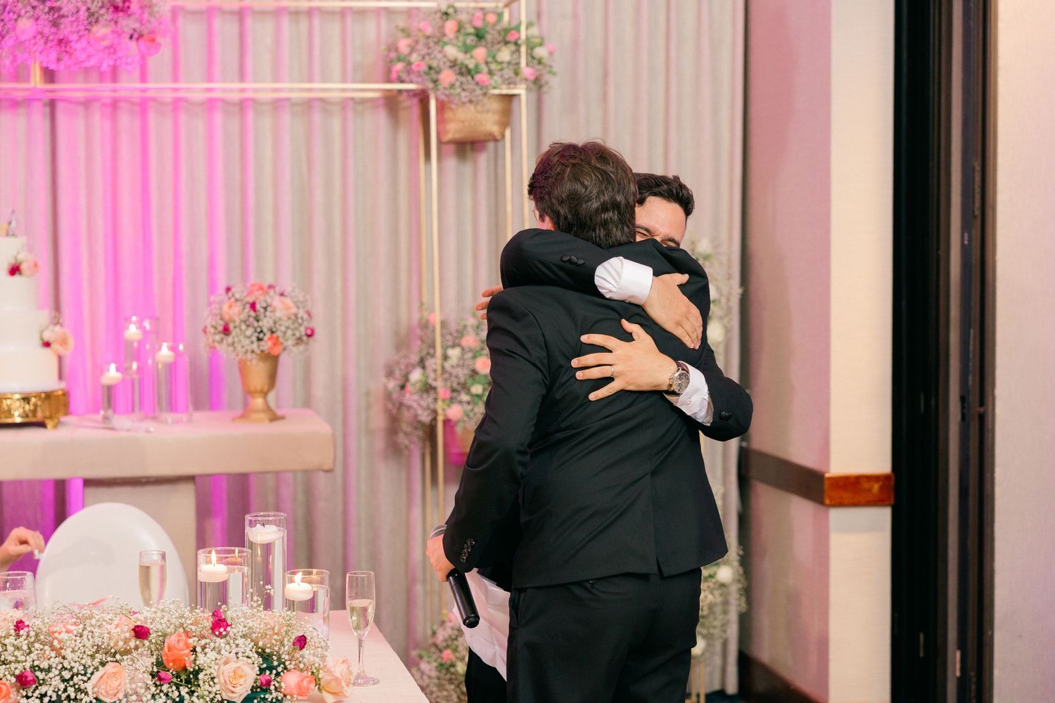 Emotional embrace between wedding guests at reception with pink decor.