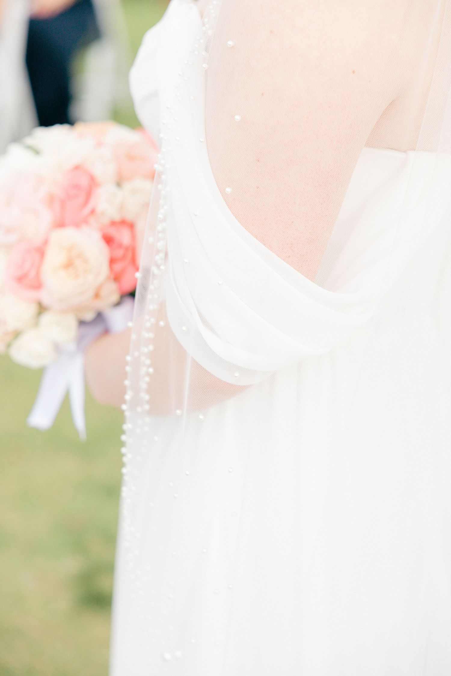 Close-up details of a white wedding dress with delicate beading and soft pink floral bouquet.
