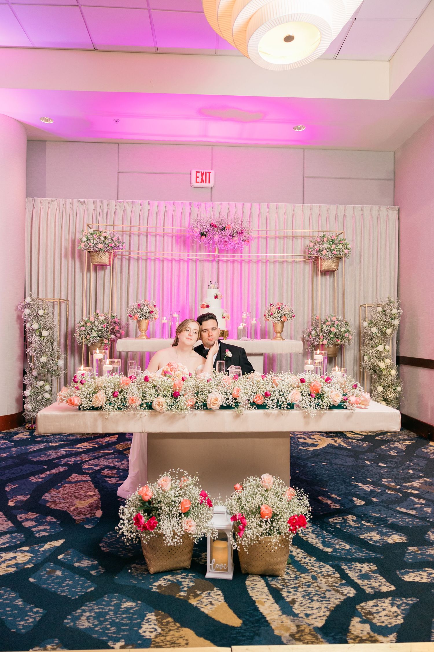 Elegant wedding reception setup with floral arrangements and pink ambient lighting.