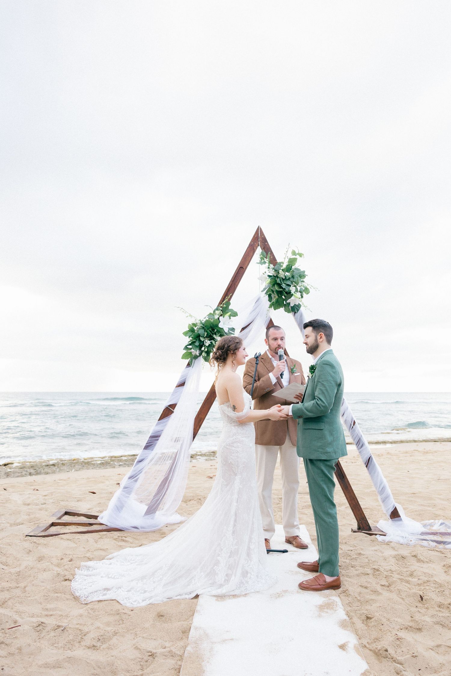 Beach wedding ceremony with white draped arch and flowing veil catching the ocean breeze.