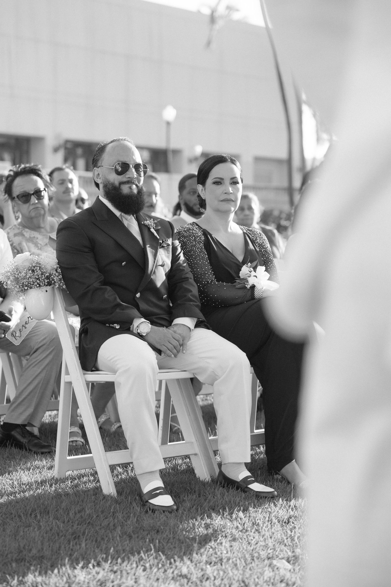 Wedding guests seated in white chairs during outdoor ceremony.