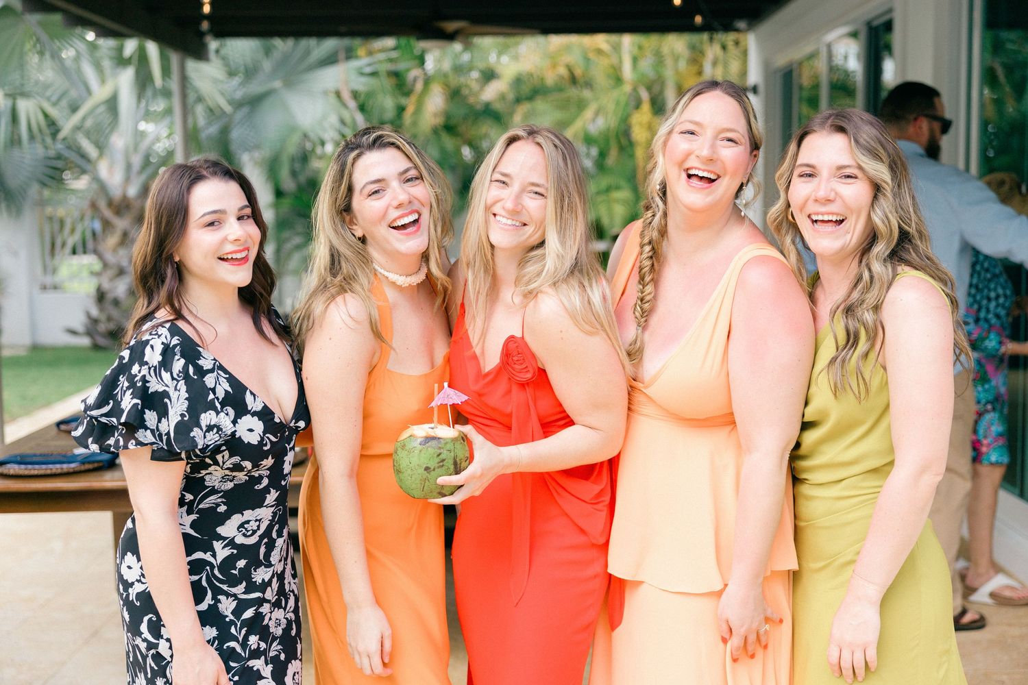 A group of friends in colorful dresses pose together at a tropical party.