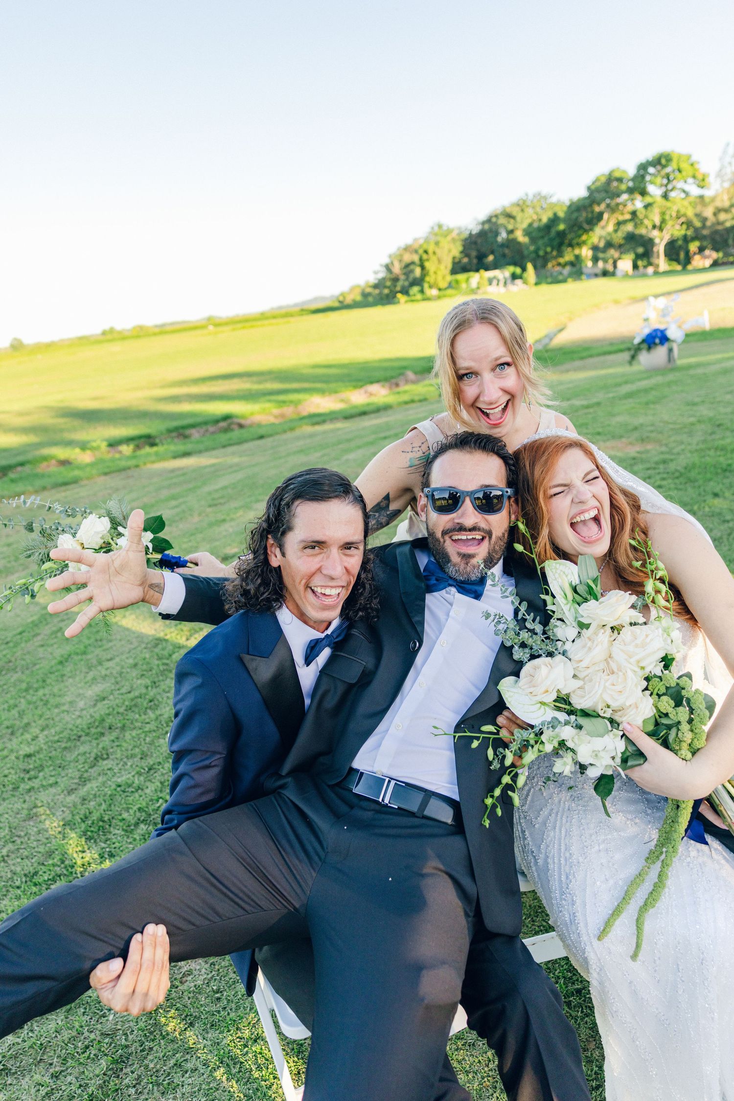 Wedding party poses playfully on green lawn during sunset photography session.