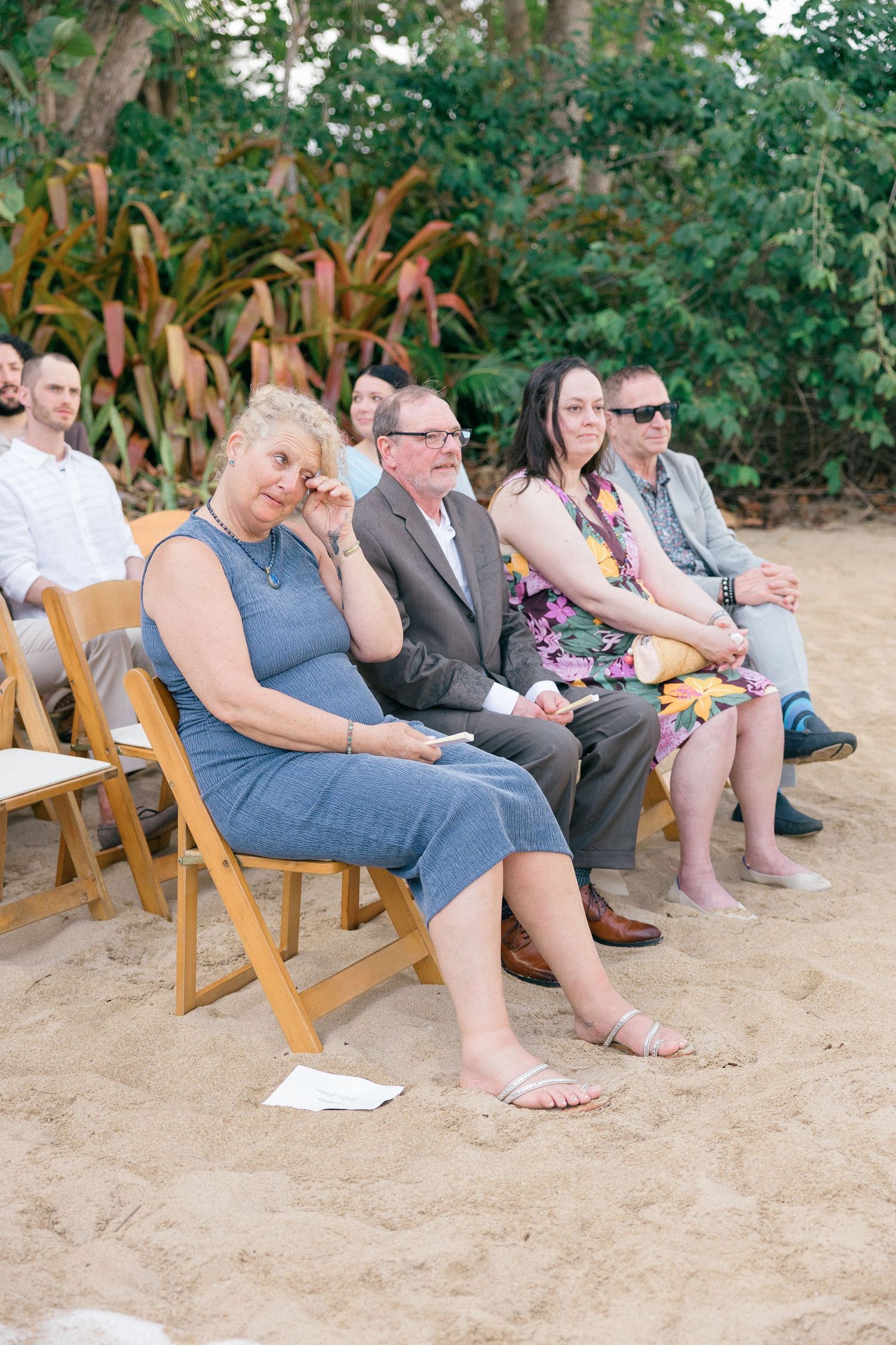 Wedding guests seated on wooden chairs at an outdoor beach ceremony.