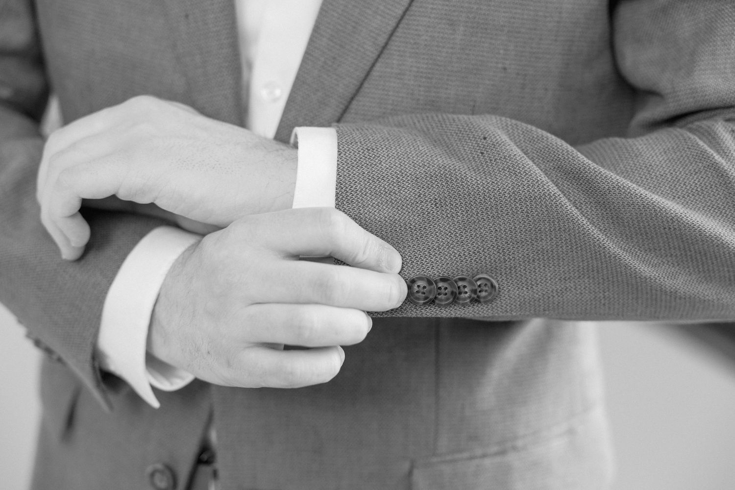 Detail shot of hands adjusting sleeve cuff on a gray suit jacket.